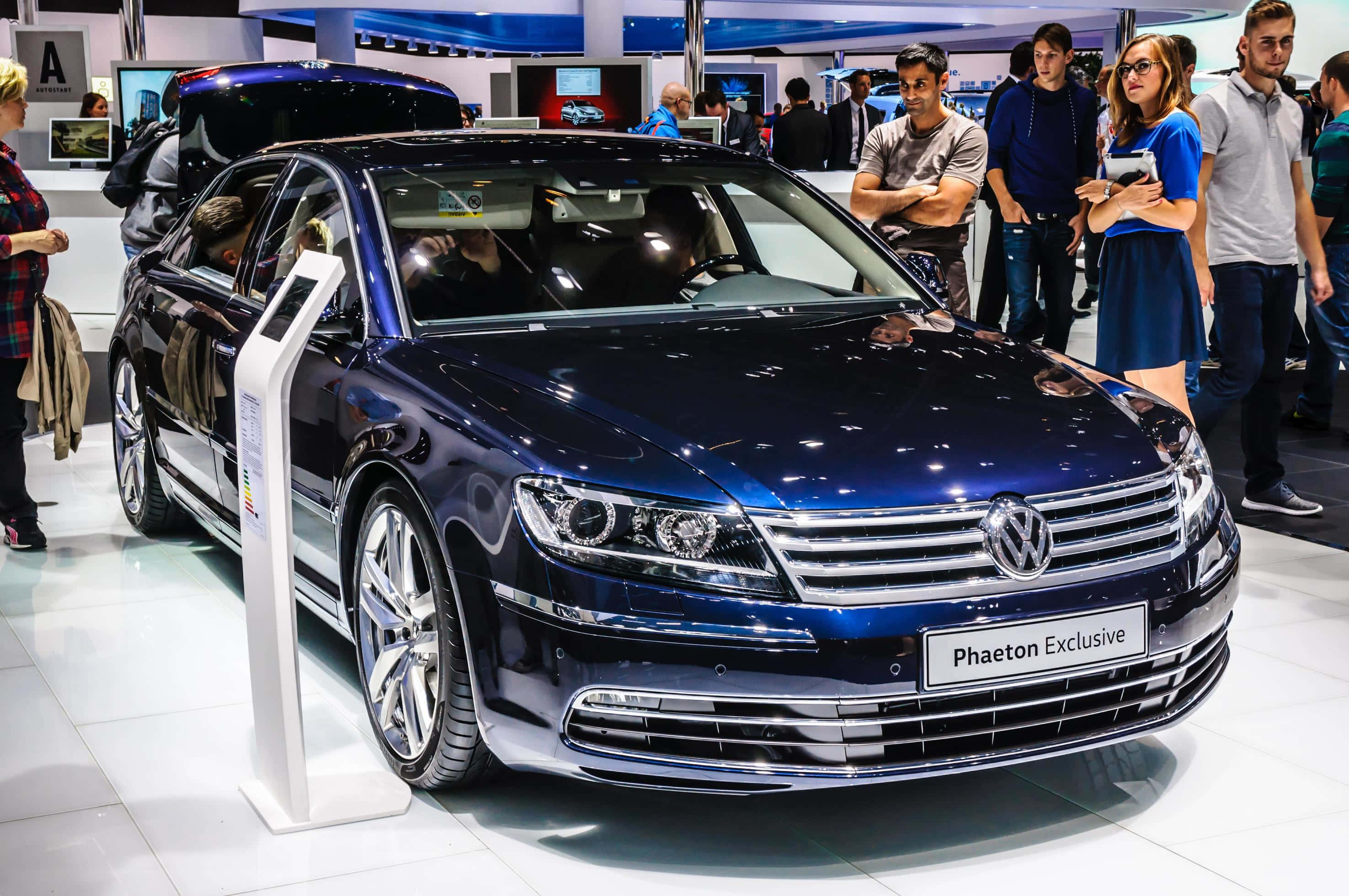 Volkswagen Phaeton 桌布 壁紙 — 一輛閃亮的藍色Volkswagen Phaeton Exclusive轎車在車展上展出，周圍有參觀者觀看。