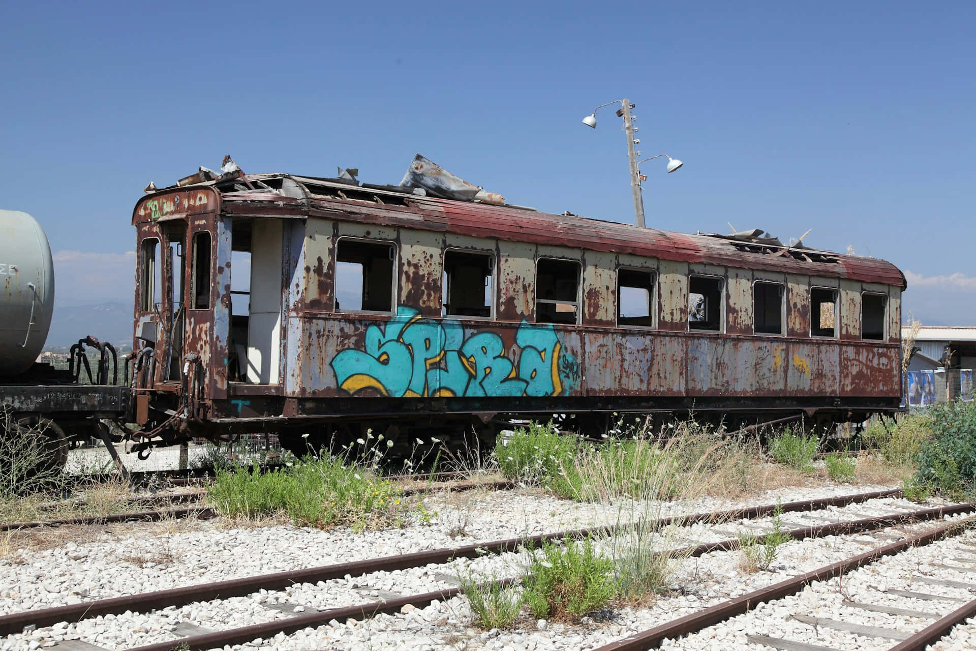  壁紙 — 一輛生鏽廢棄的火車車廂帶有藍色塗鴉，停在長滿雜草的軌道上，天空清澈湛藍。