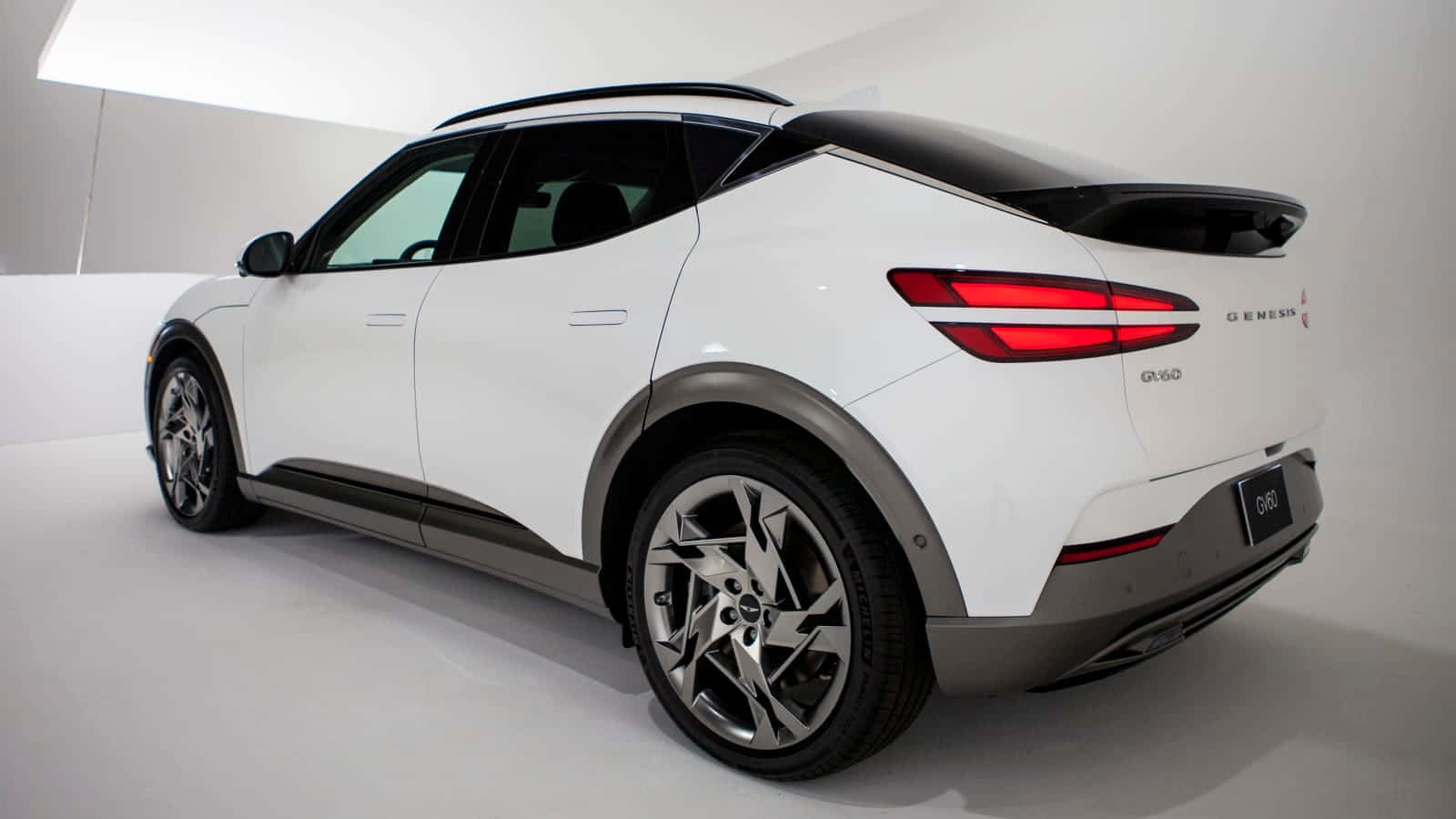 白色 Genesis GV60 電動 SUV 在工作室中，帶有紅色尾燈和鍍鉻輪圈。 — Toyota Supra Mk4 壁紙