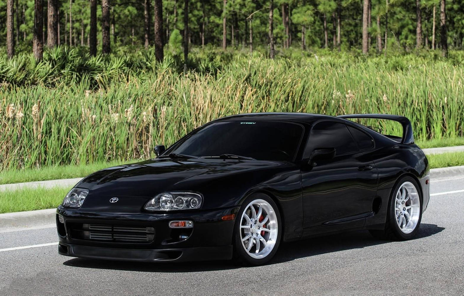 黑色豐田Supra跑車停靠在靠近草地森林的道路上。 — Toyota Supra 壁紙