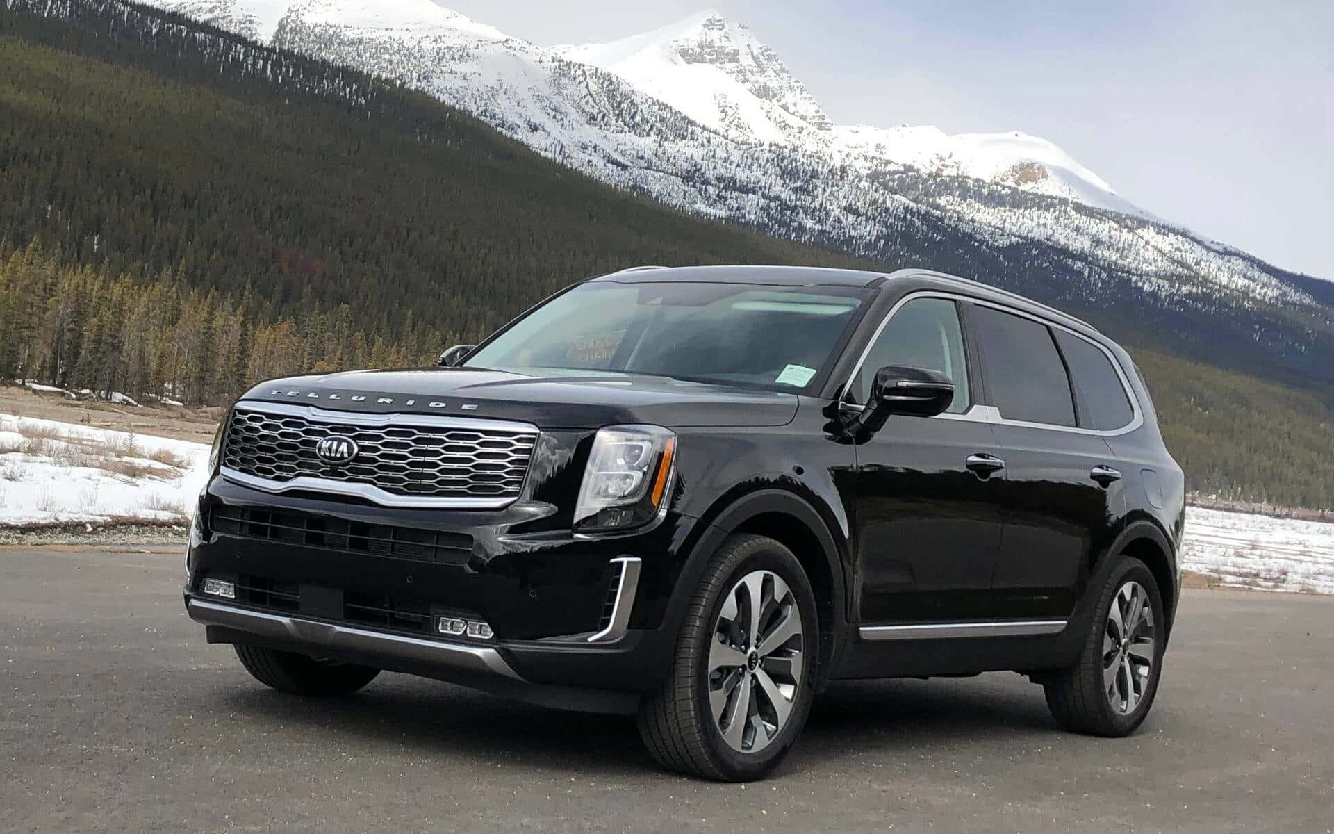 Kia Telluride 桌布 壁紙 — 一輛時尚的黑色Kia Telluride SUV停在人行道上，背景是白雪覆蓋的山脈和常綠森林。