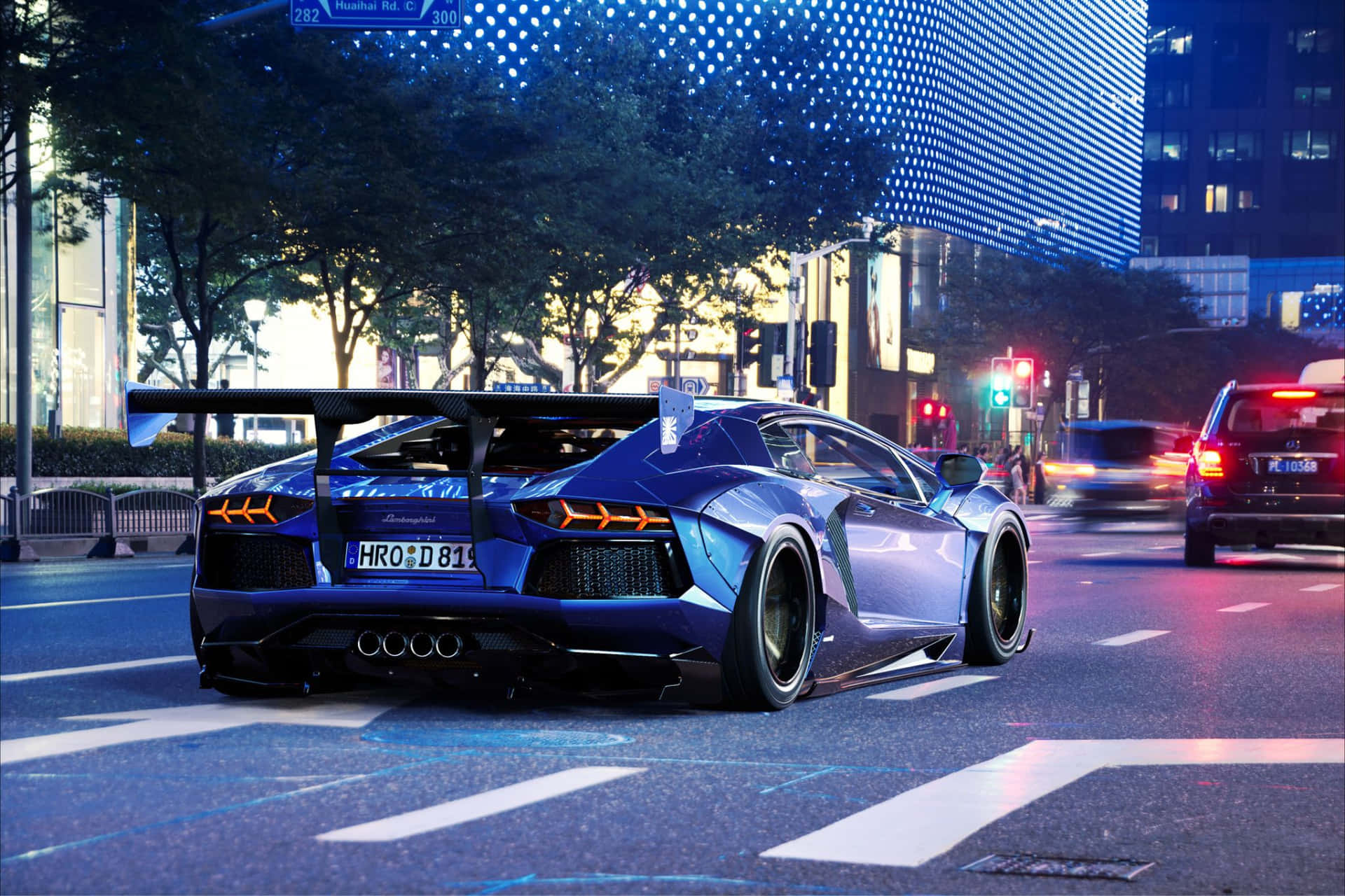  壁紙 — 一輛時尚的藍色藍寶堅尼 Aventador SVJ 在黃昏時分，穿過霓虹燈照亮的大街，車輪留下動態模糊的軌跡。