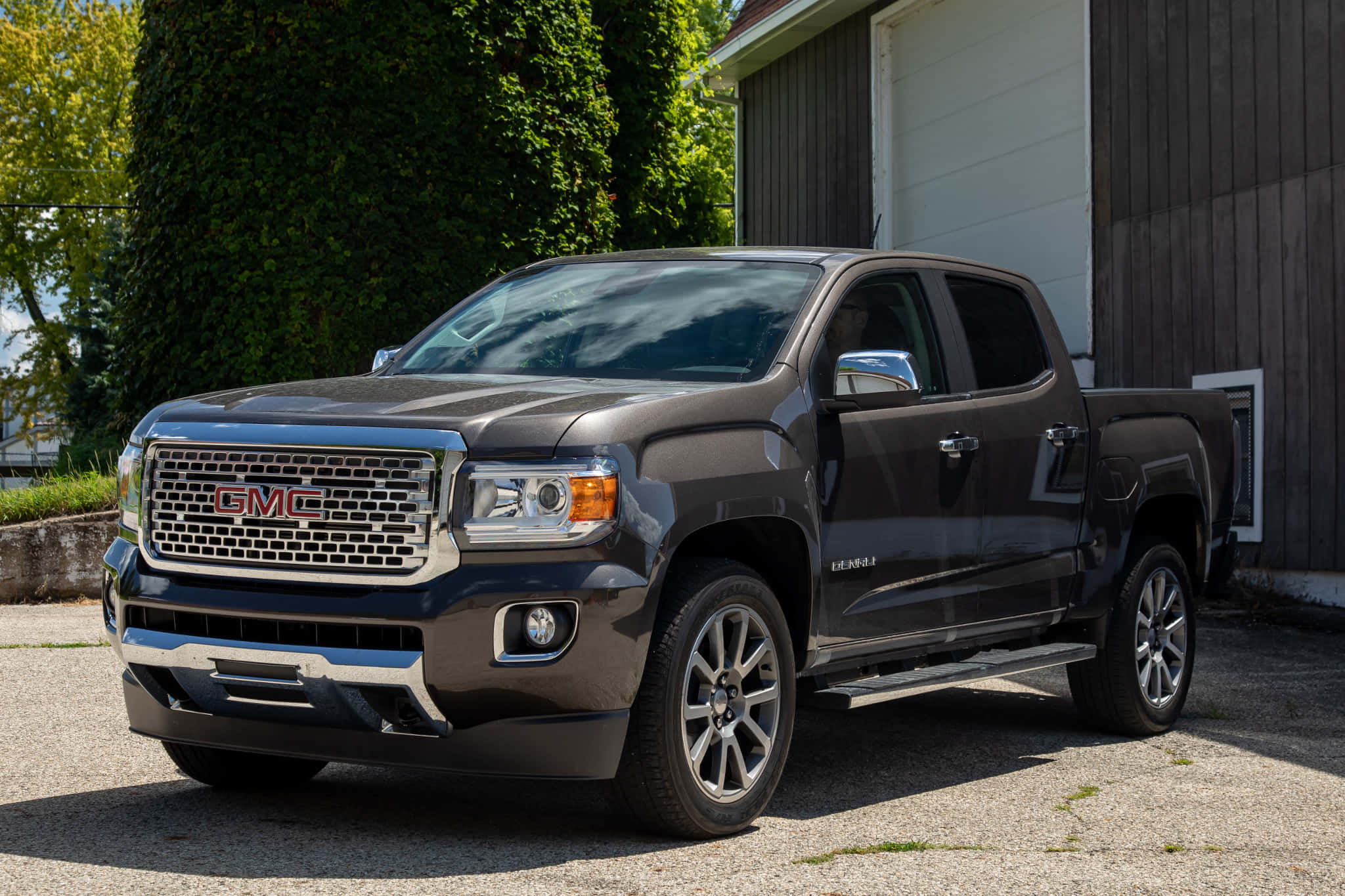 Gmc Canyon 桌布 壁紙 — 一輛時尚的深灰色 GMC Canyon 皮卡車停在碎石上，旁邊是木製車庫，牆上爬滿常春藤，在明亮的日光下。