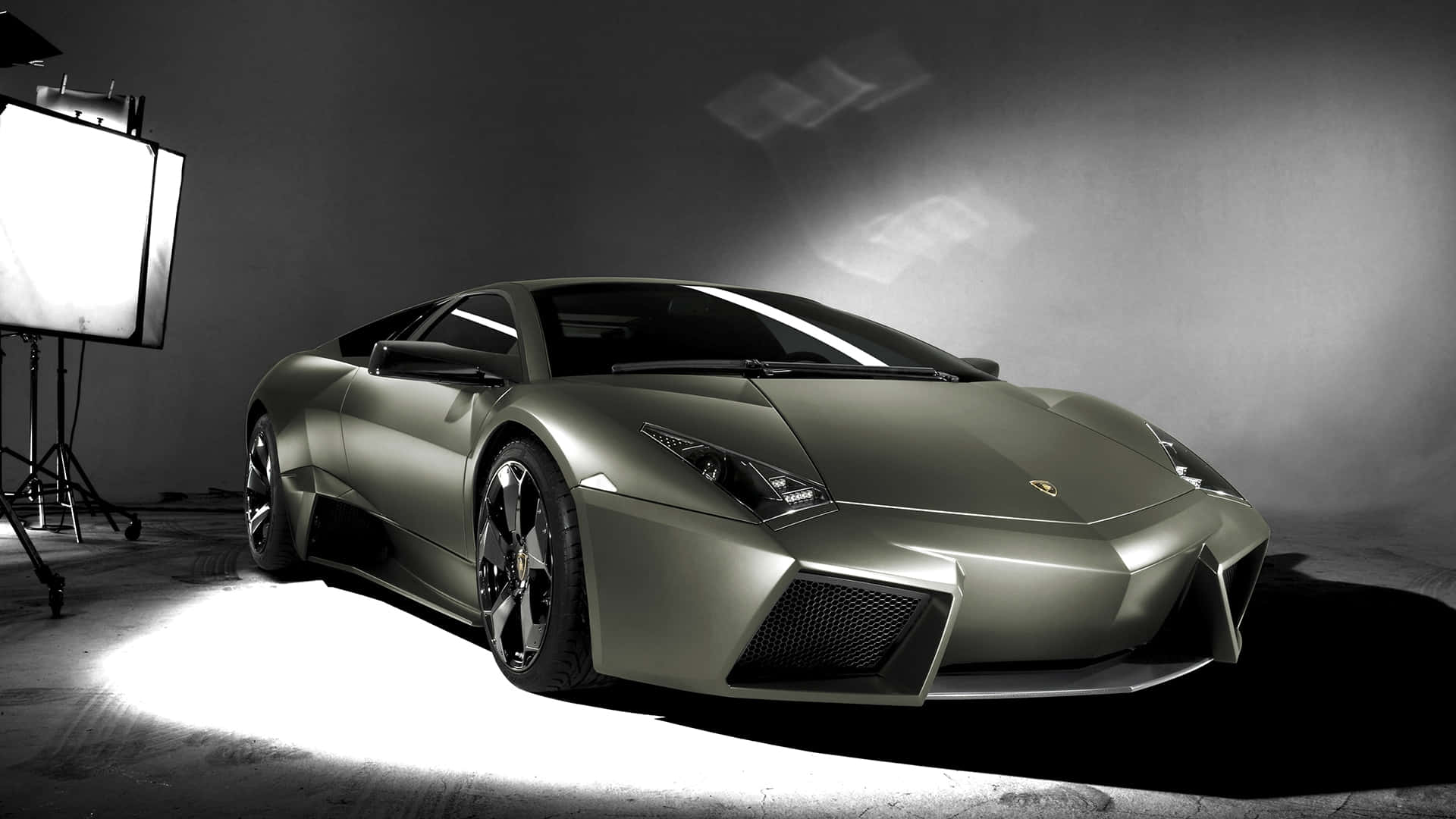 Lamborghini Reventón 桌布 壁紙 — 一輛時尚的啞光綠色藍寶堅尼跑車在攝影棚內被戲劇性地照亮，可見的照明設備投射出銳利的陰影。