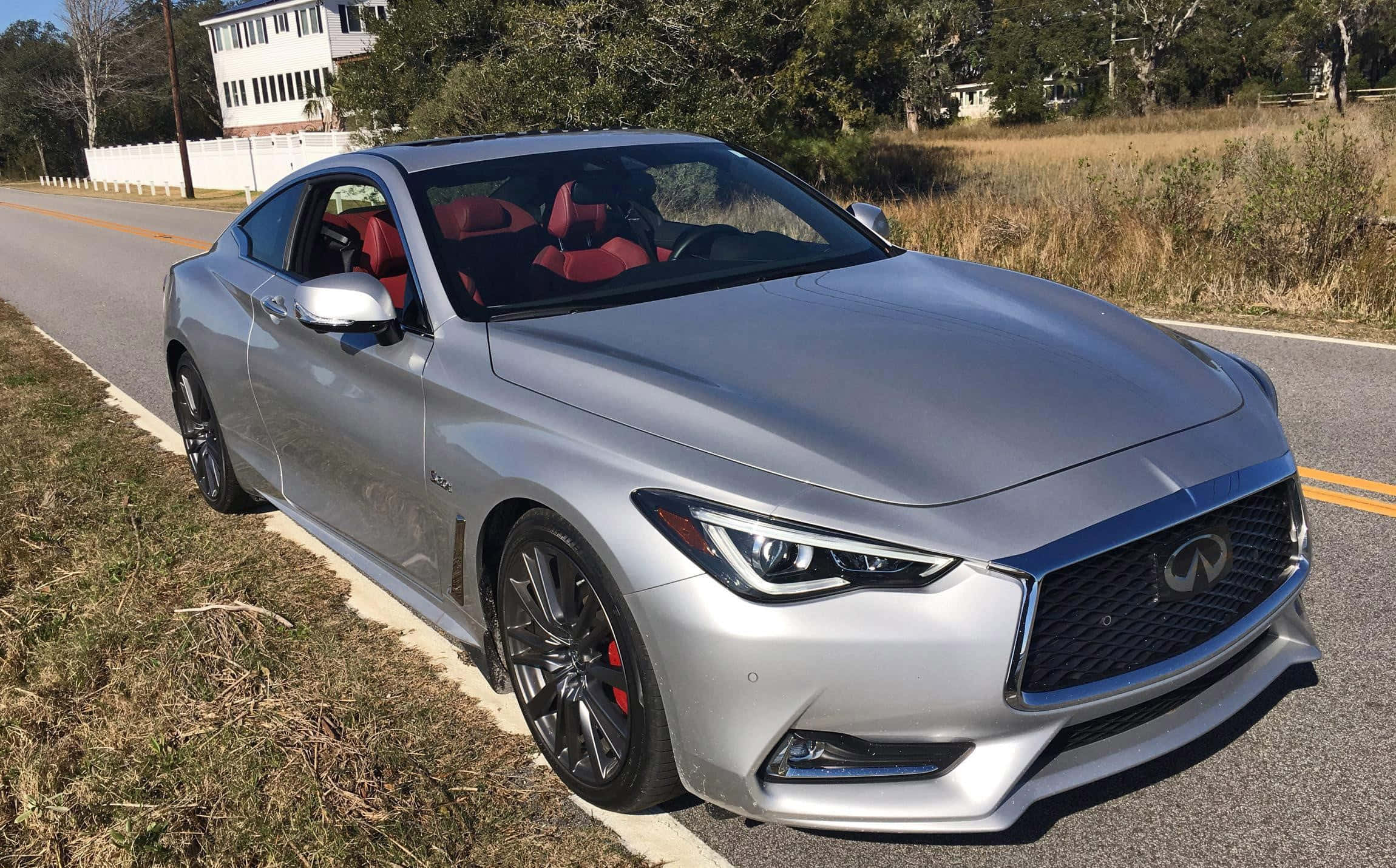 Infiniti Q60 桌布 壁紙 — 一輛時尚的銀色Infiniti Q60跑車，紅色內裝，停在路邊，背景有乾草和樹木。