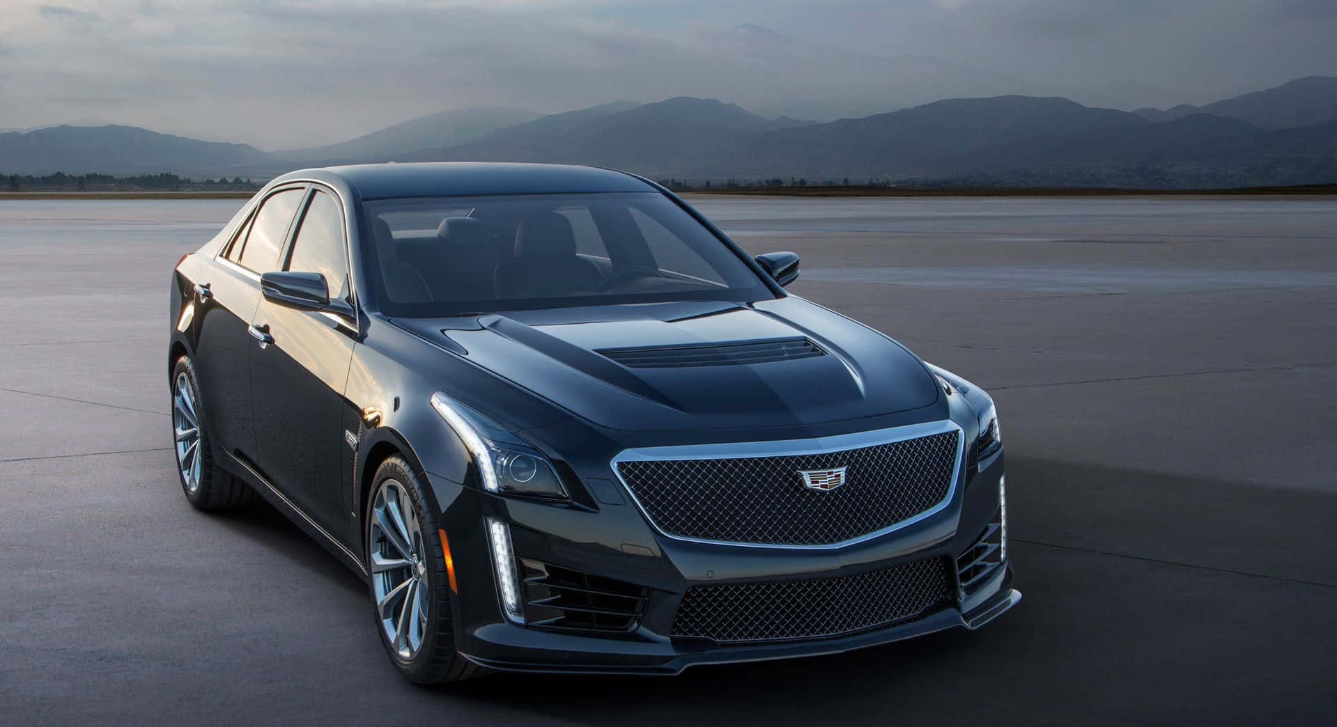 Cadillac Cts 桌布 壁紙 — 一輛時尚的黑色Cadillac CTS-V轎車在柔和的暮光下，在廣闊的混凝土場地上閃耀，遠山為背景。