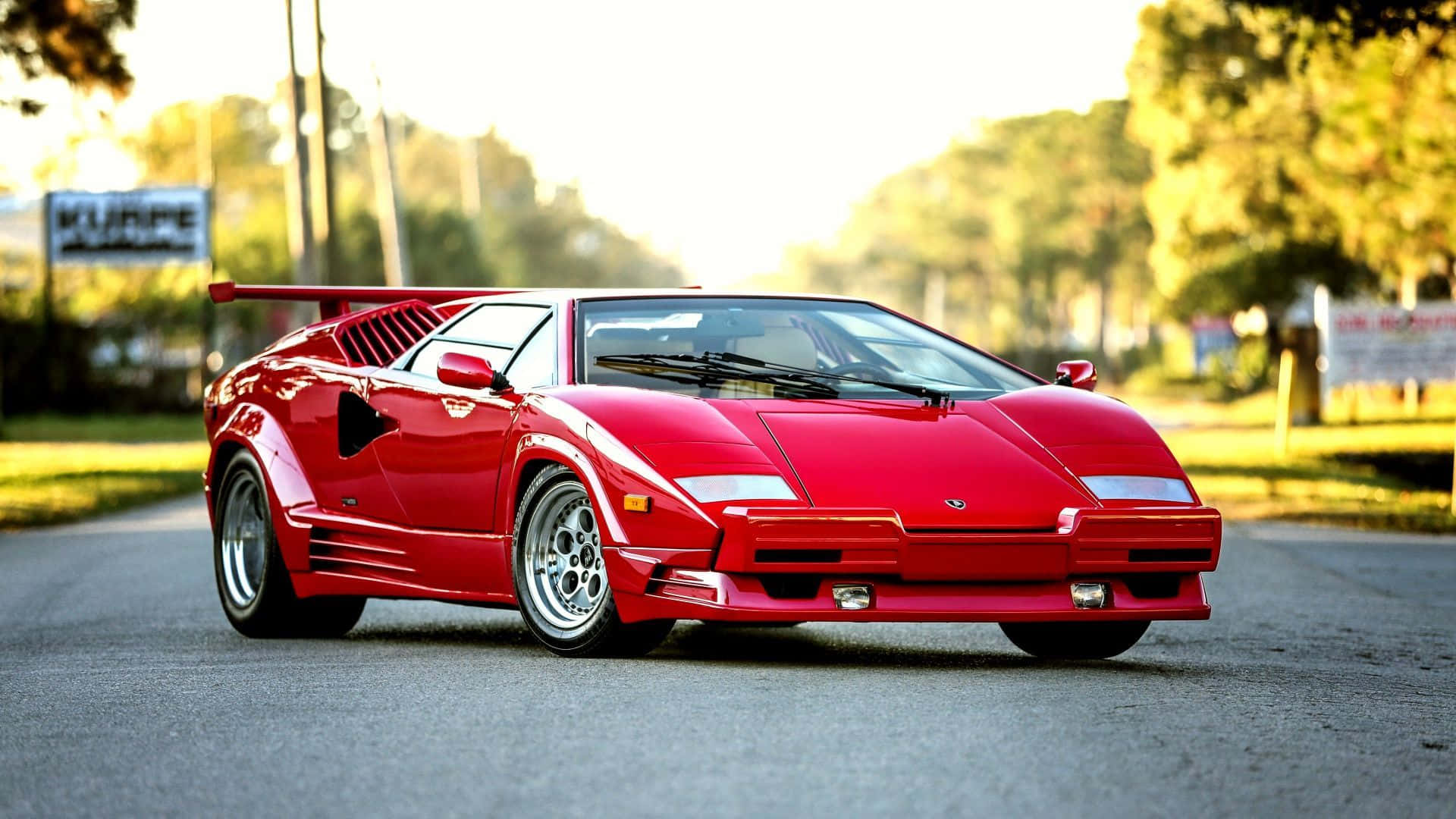 Lamborghini Countach 桌布 壁紙 — 一輛鮮紅色的藍寶堅尼Countach停泊在陽光普照的道路上，背景有樹木和柔和的金色光線。