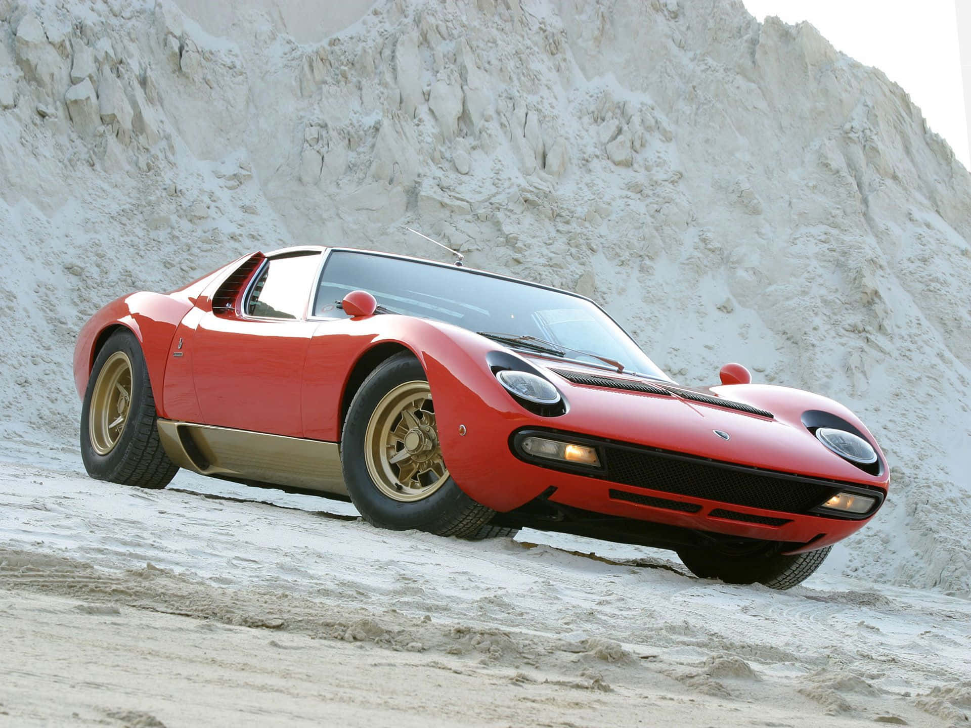 Lamborghini Miura 桌布 壁紙 — 一輛鮮紅色的藍寶堅尼Miura跑車停泊在崎嶇的白色沙坡上，背景是高聳的懸崖峭壁。