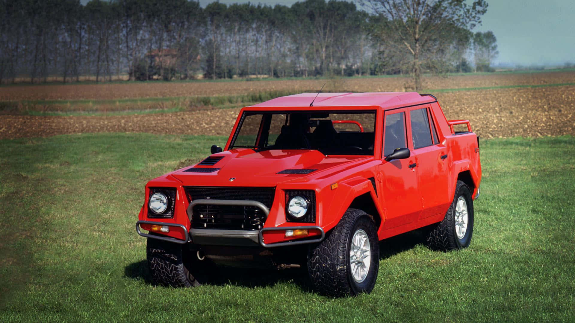 Lamborghini Lm002 桌布 壁紙 — 一輛醒目的紅色藍寶堅尼LM002大膽地停在草地上，背景是樹木和農田，天空晴朗。