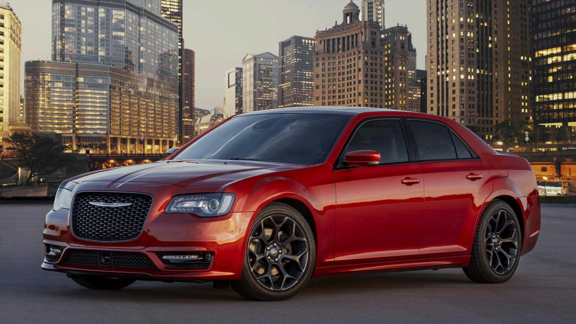 Chrysler 300 桌布 壁紙 — 一輛光澤的紅色克萊斯勒轎車，配黑色輪圈，停泊在黃金時段的城市天際線前。