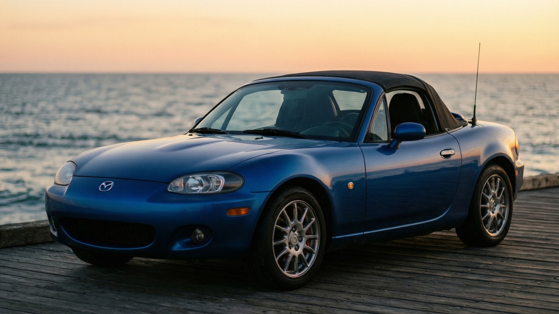 Pier Sunset Miata NC 壁紙 — 一輛藍色馬自達MX-5敞篷車停泊在日落時分的木製碼頭上，背景有海浪。