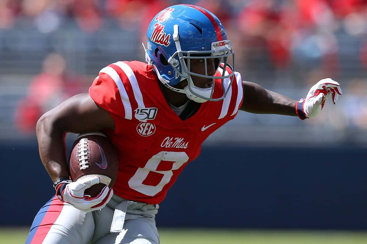  壁紙 — 一名身穿紅色 Ole Miss 球衣的足球員在明亮的日間比賽中帶球衝刺。