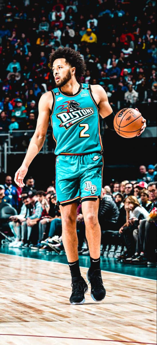  壁紙 — 一名身穿青綠色Pistons球衣的籃球運動員在比賽中運球，背景是座無虛席的體育館。