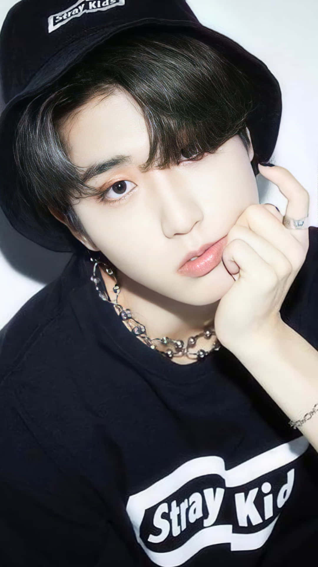  壁紙 — 一名戴黑色漁夫帽、身穿Stray Kids T恤的年輕男子，在純白背景前將手靠近臉部擺姿勢。