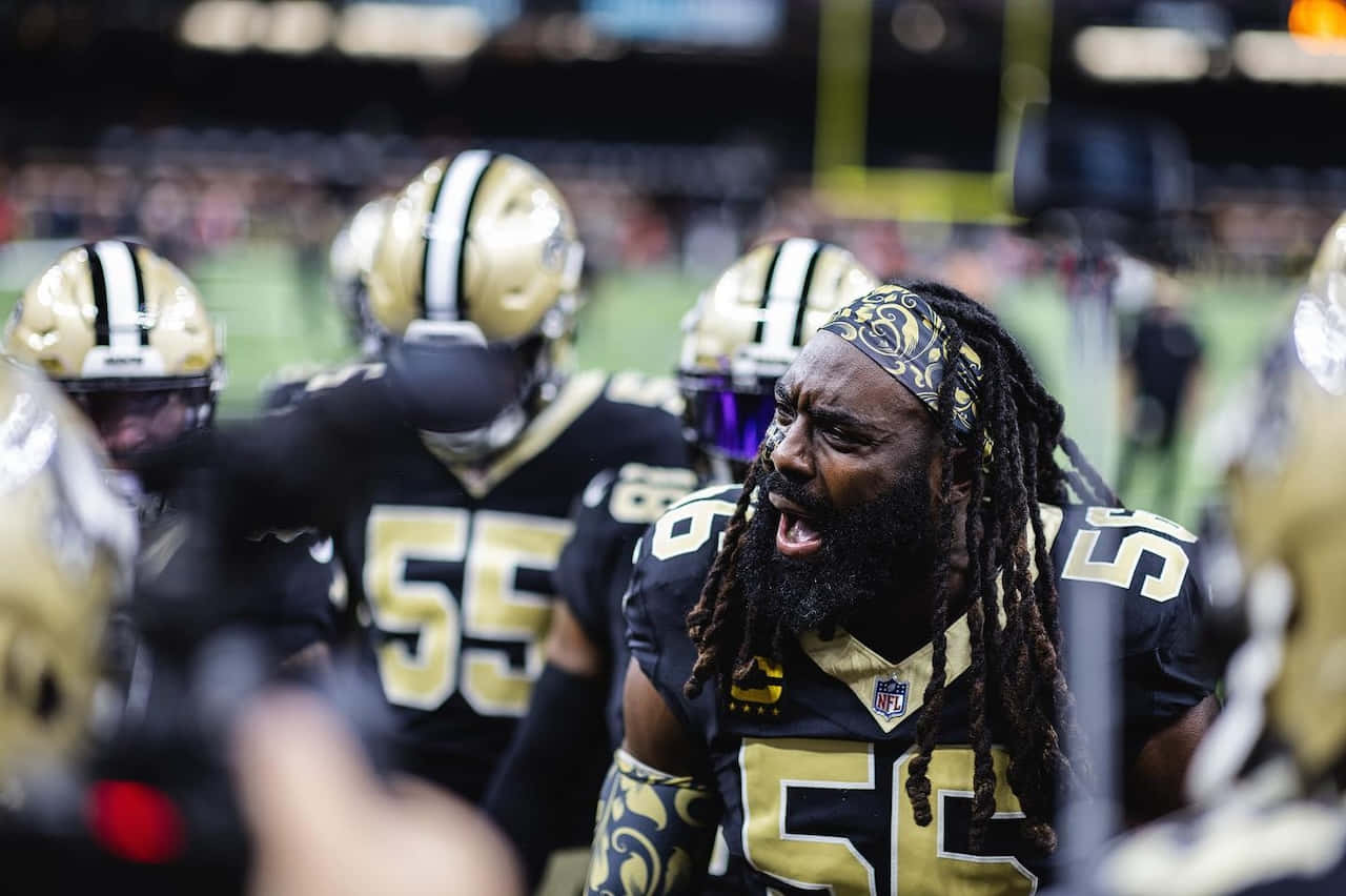 壁紙 — 一名帶有辮子頭和金色頭盔的激烈NFL球員在球場燈光下比賽中大喊的特寫。