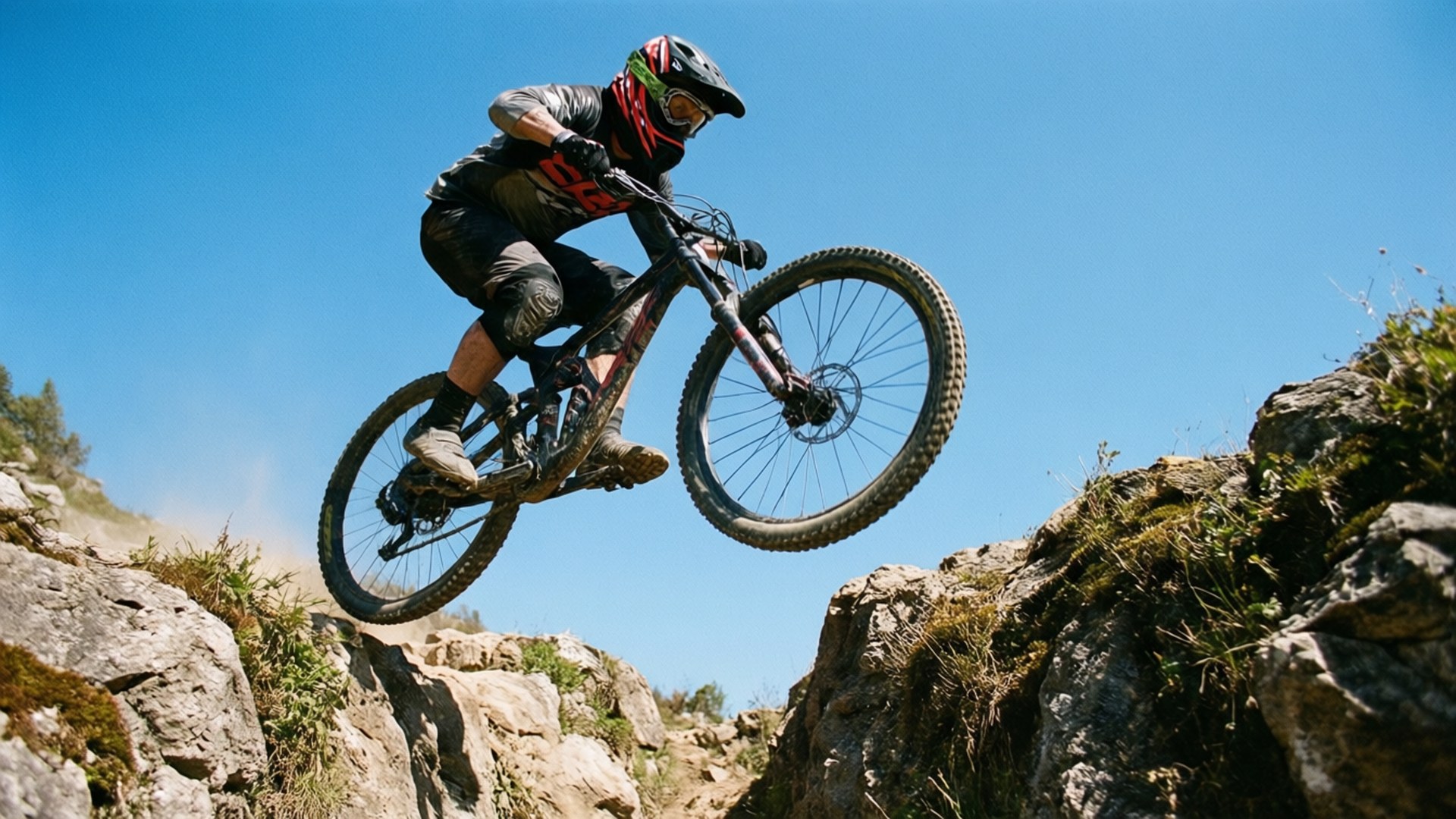 Jump Over Gap 壁紙 — 一名登山車手在晴朗的藍天下，飛越岩石地形上空。