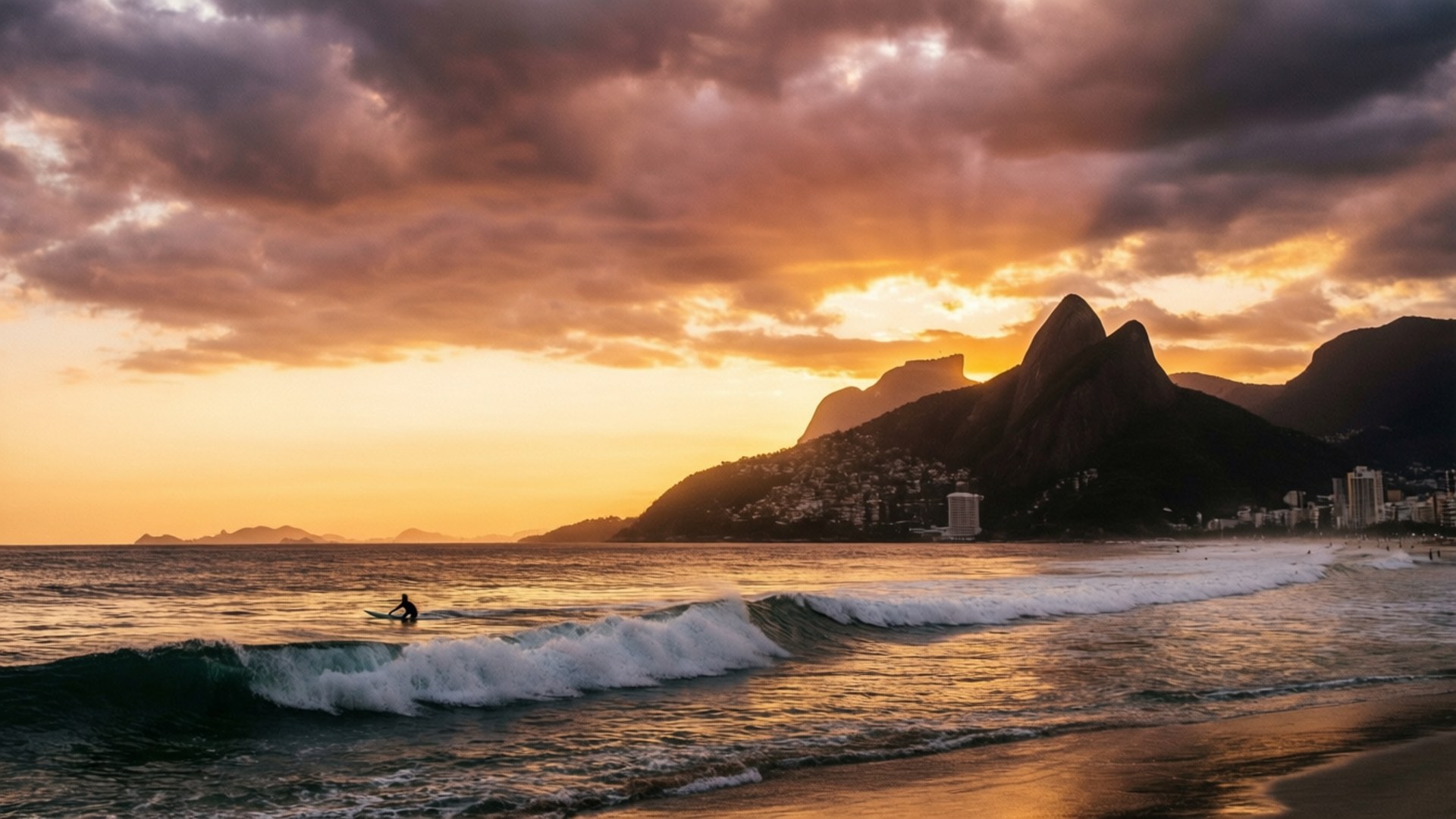 Ipanema Sunset Surfer 壁紙 — 一名孤獨的衝浪者在日落時分乘風破浪，背後是戲劇性的橙色雲彩和剪影般的山脈，以及一個海灘小鎮。