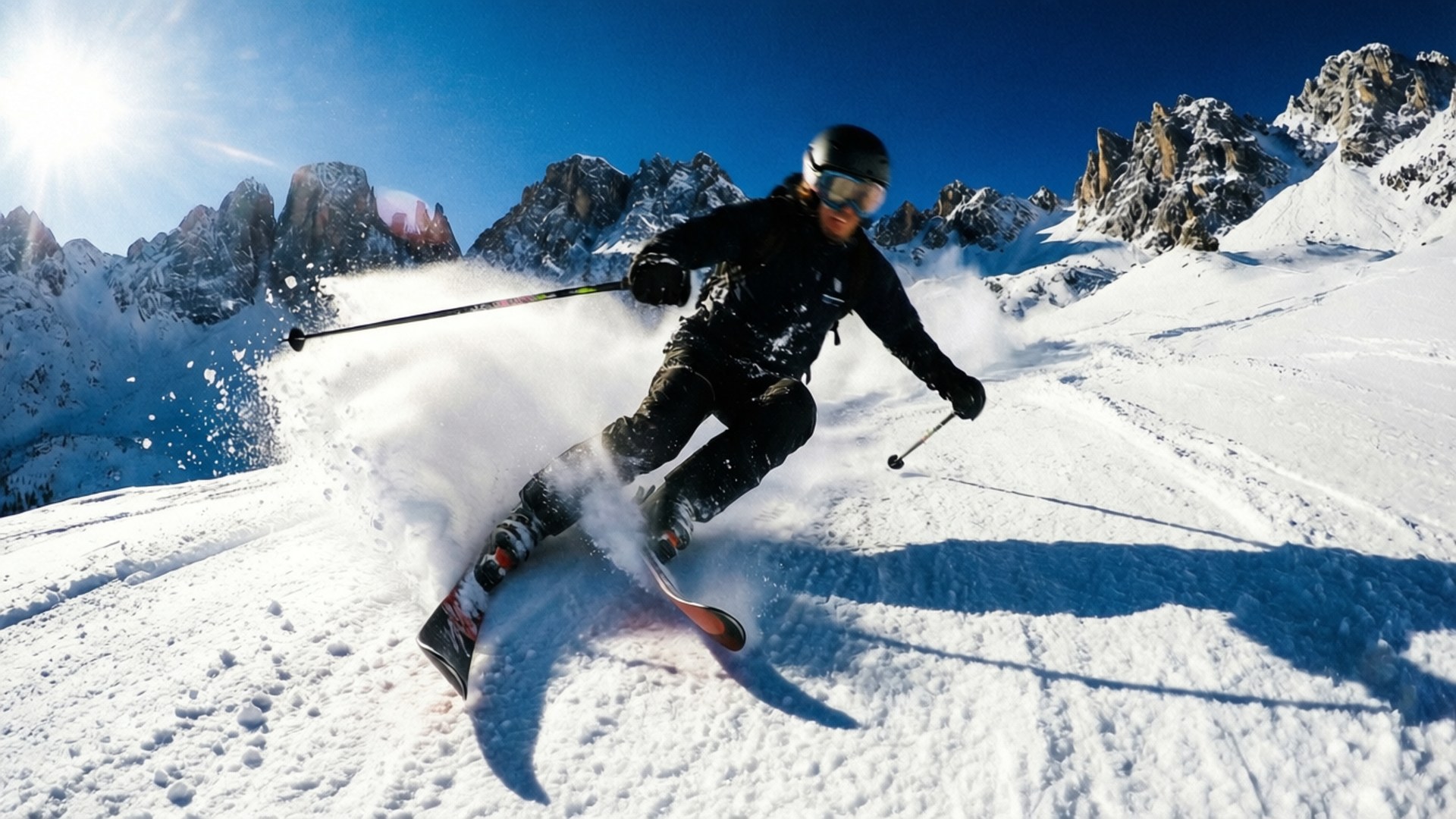 ski 桌布 壁紙 — 一名滑雪者在陽光明媚的山坡上穿過新鮮的粉雪，背景是鋸齒狀的山峰。