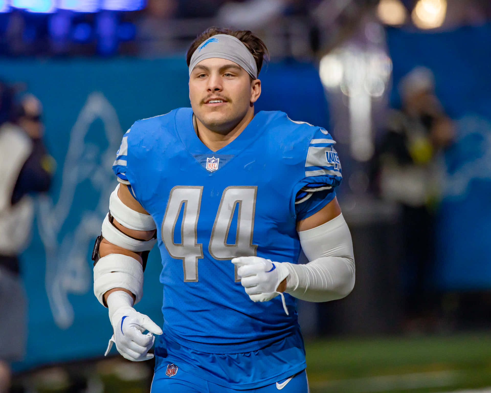  壁紙 — 一名堅定的NFL球員身穿藍色球衣，號碼44，在明亮的燈光下於體育場奔跑。