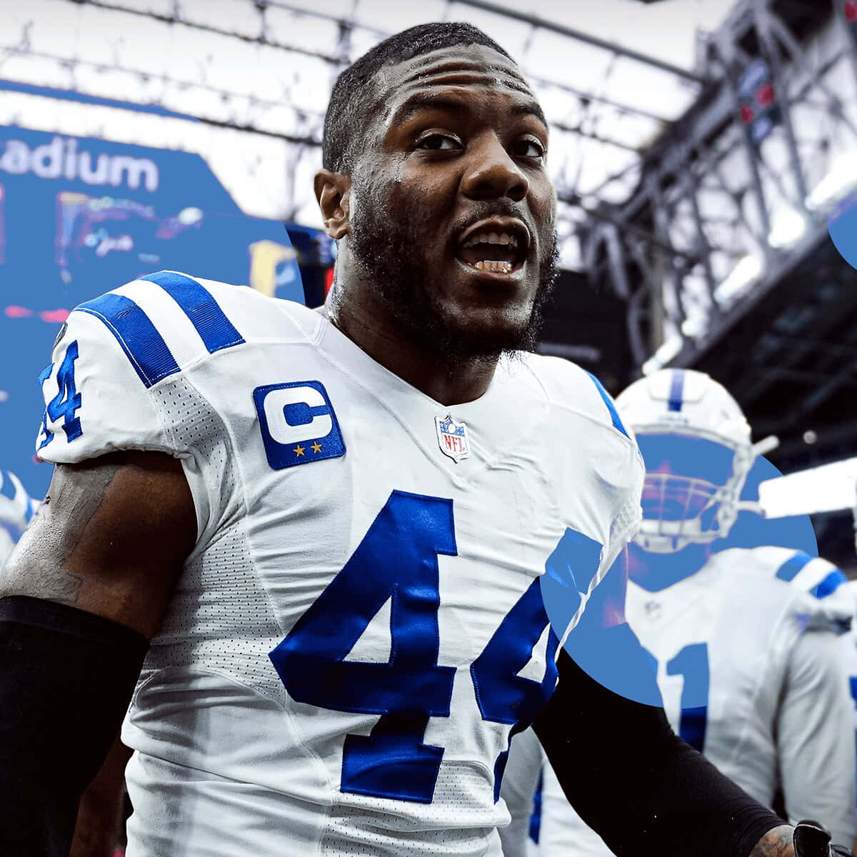  壁紙 — 一名決心堅定的NFL球員，身穿白色和藍色制服，號碼44，帶有隊長臂章，站在體育場球場上的特寫。