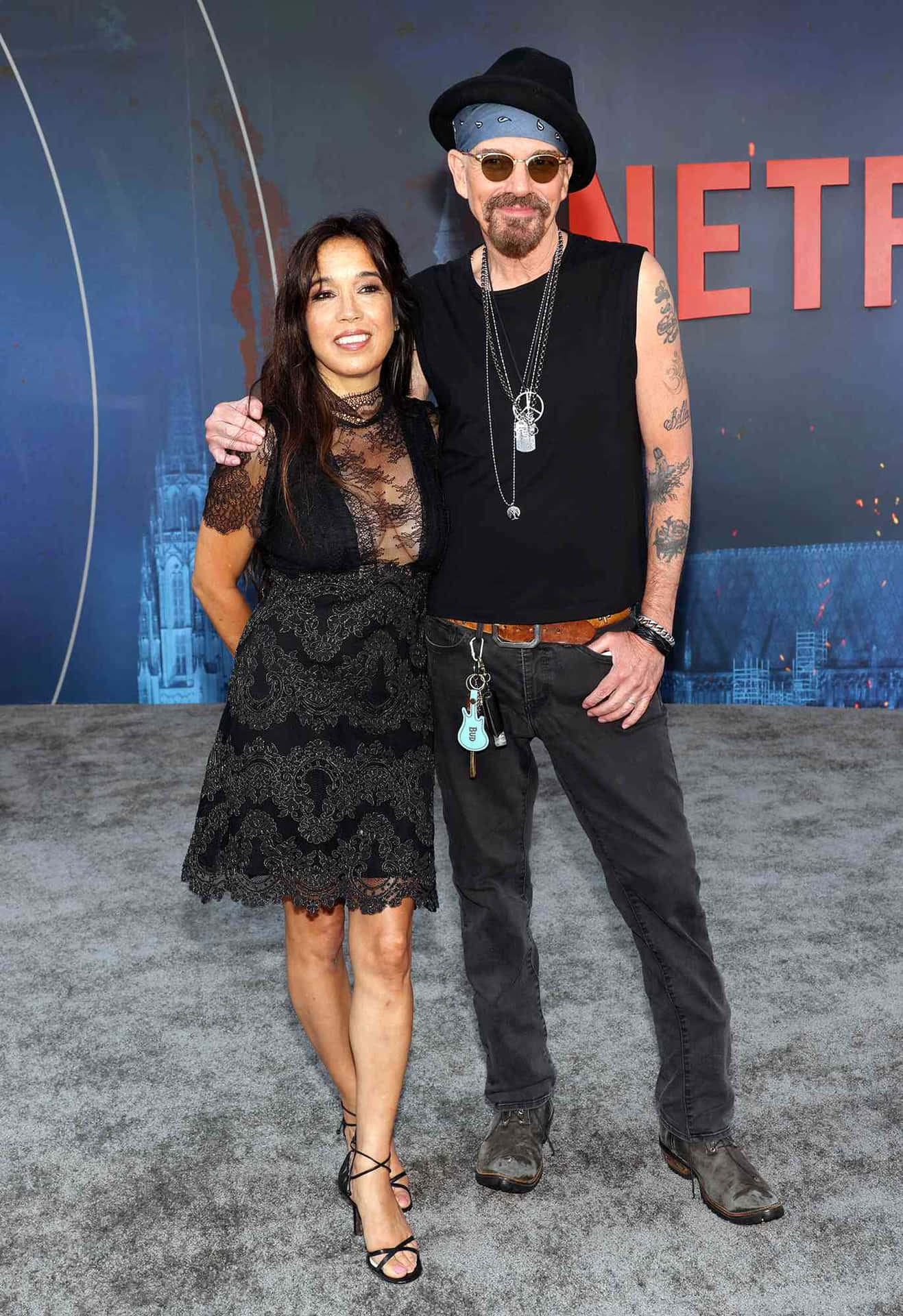  壁紙 — 一名男子和一名女子在灰色地毯上，於藍色Netflix背景前合照，背景有城市景觀圖案。