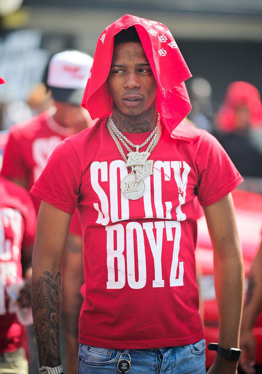  壁紙 — 一名年輕男子穿著紅色頭巾連帽衫和相配的紅色'SOICY BOYZ' T恤，帶有刺青和層疊金鍊，自信地站立。