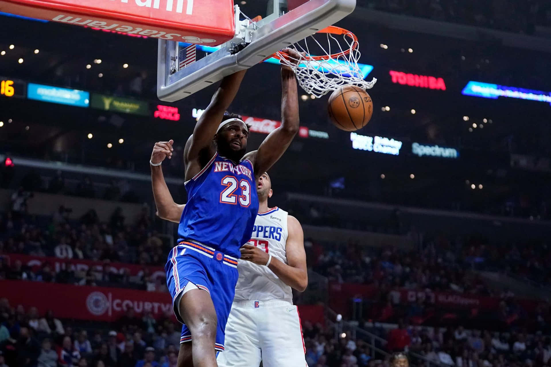 籃球運動員在擠滿觀眾的場館中越過防守球員灌籃。 — NBA 壁紙
