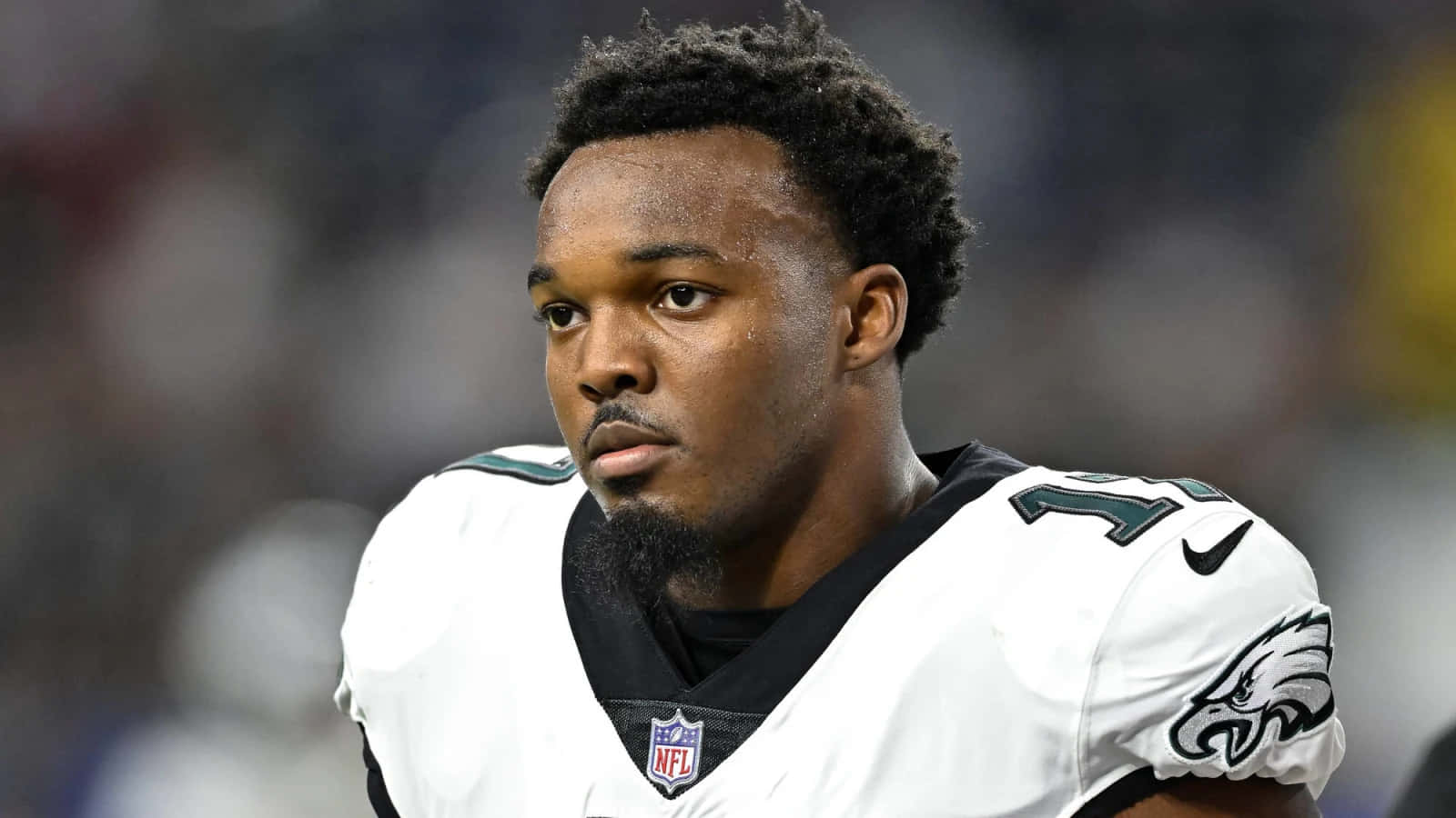  壁紙 — 一名身穿白色老鷹隊球衣、專注的NFL美式足球員在球場燈光下比賽時凝視著。