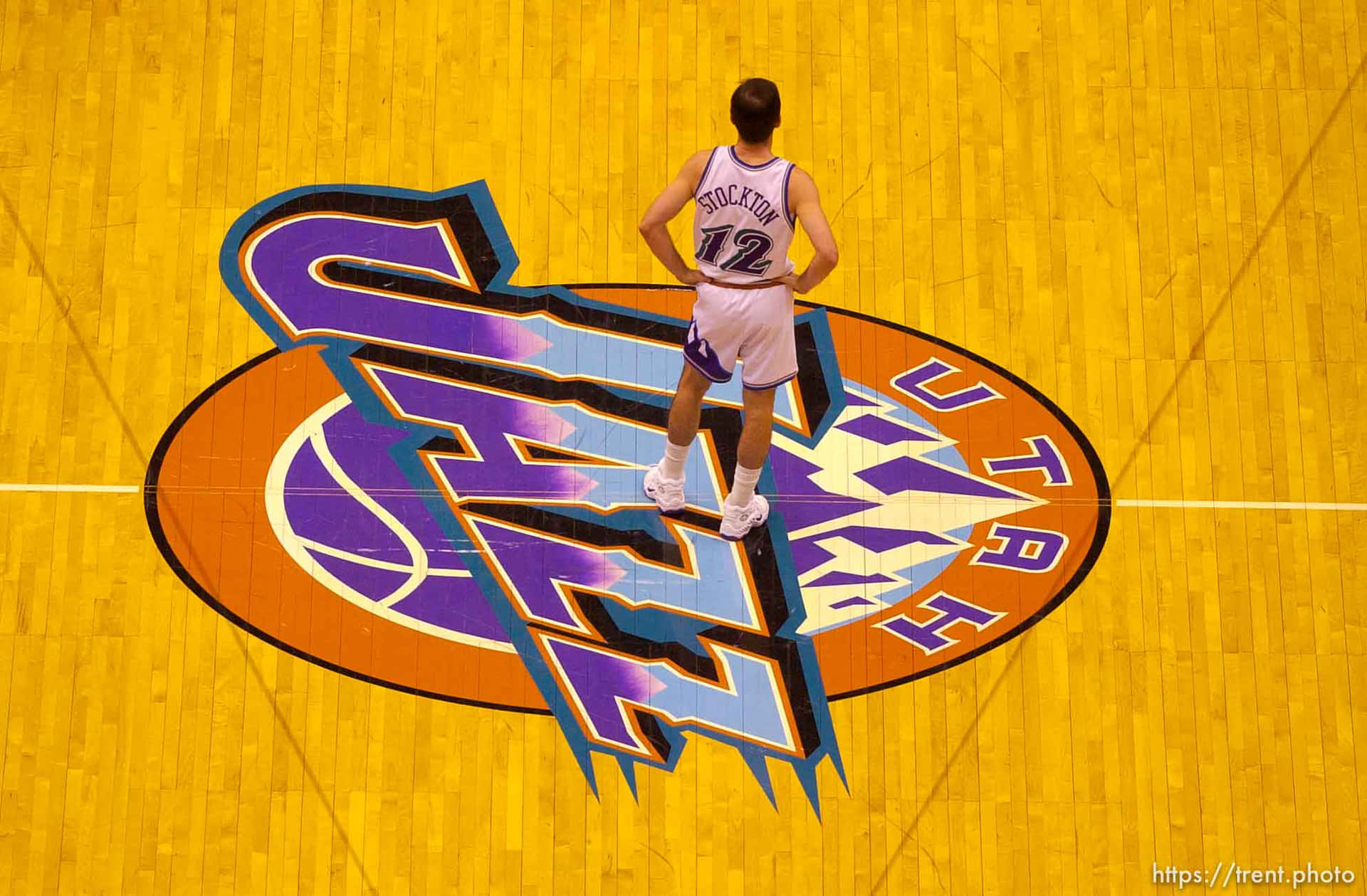 白色球衣籃球運動員站在黃色球場的猶他爵士隊標誌上。 — NBA 壁紙