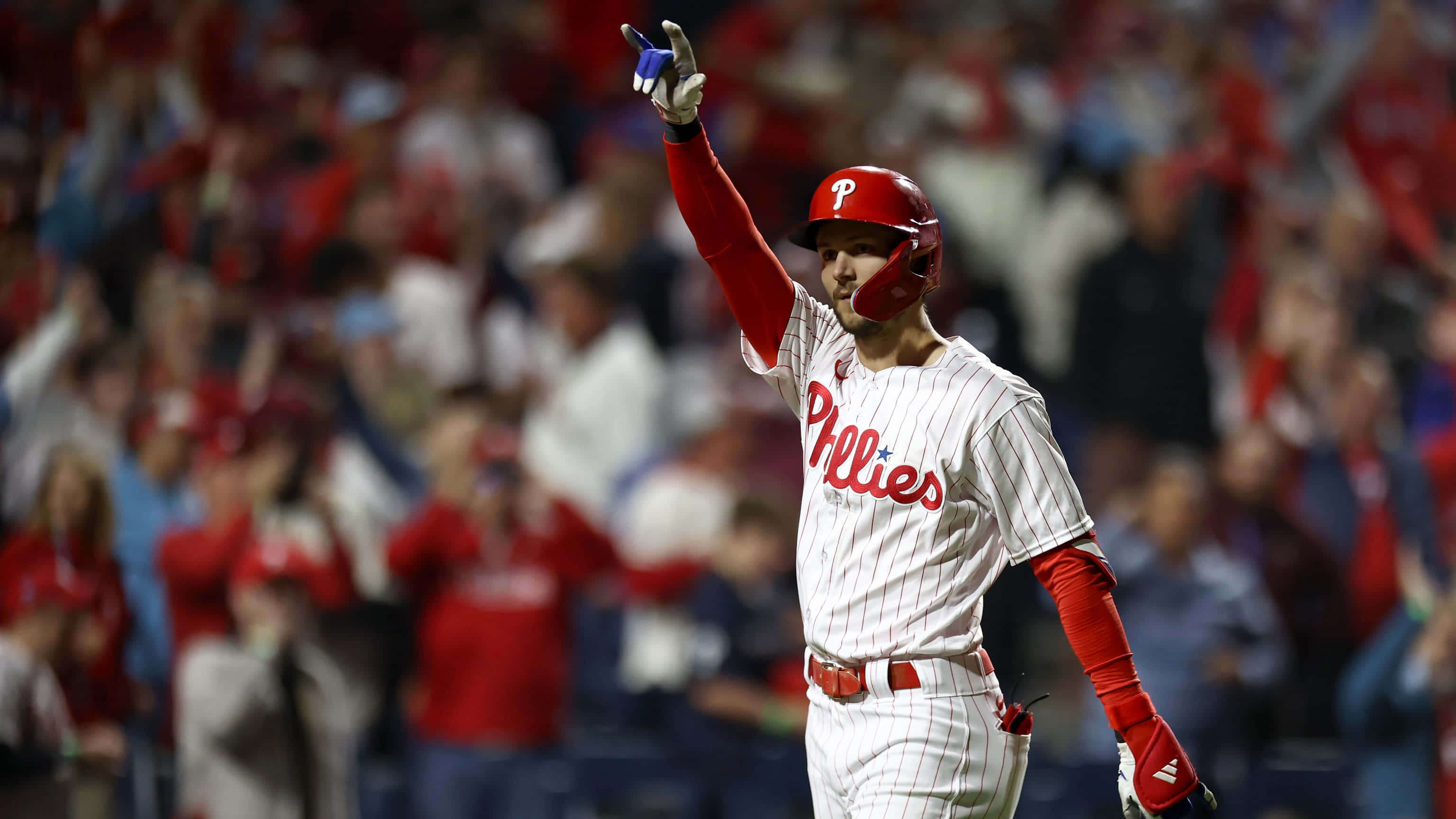 Trea Turner Phillies 桌布 壁紙 — 一名身穿白色細條紋球衣的費城費城人棒球選手，在球迷歡呼聲中高舉戴著手套的手慶祝勝利。