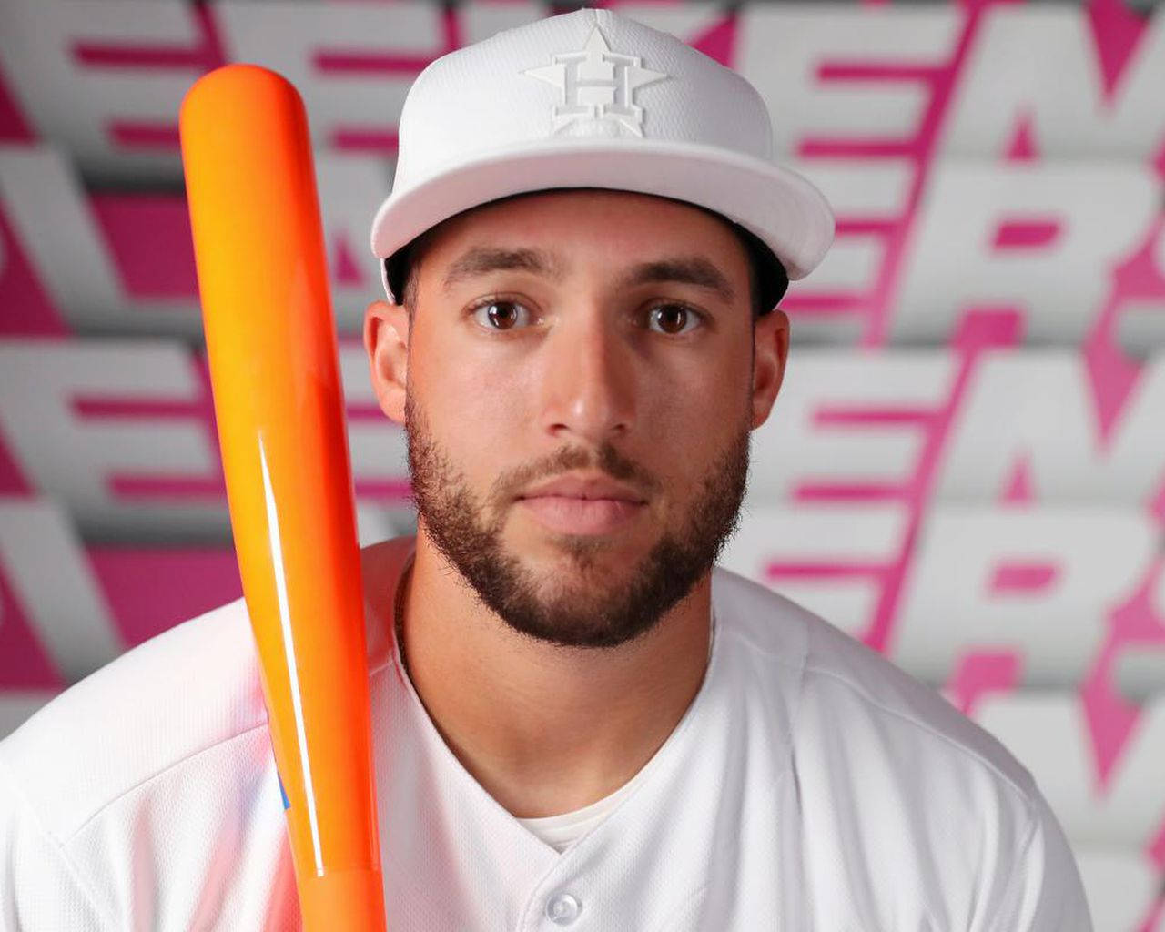 棒球運動員在粉紅色幾何背景的工作室中握著橙色球棒。 — MLB 壁紙