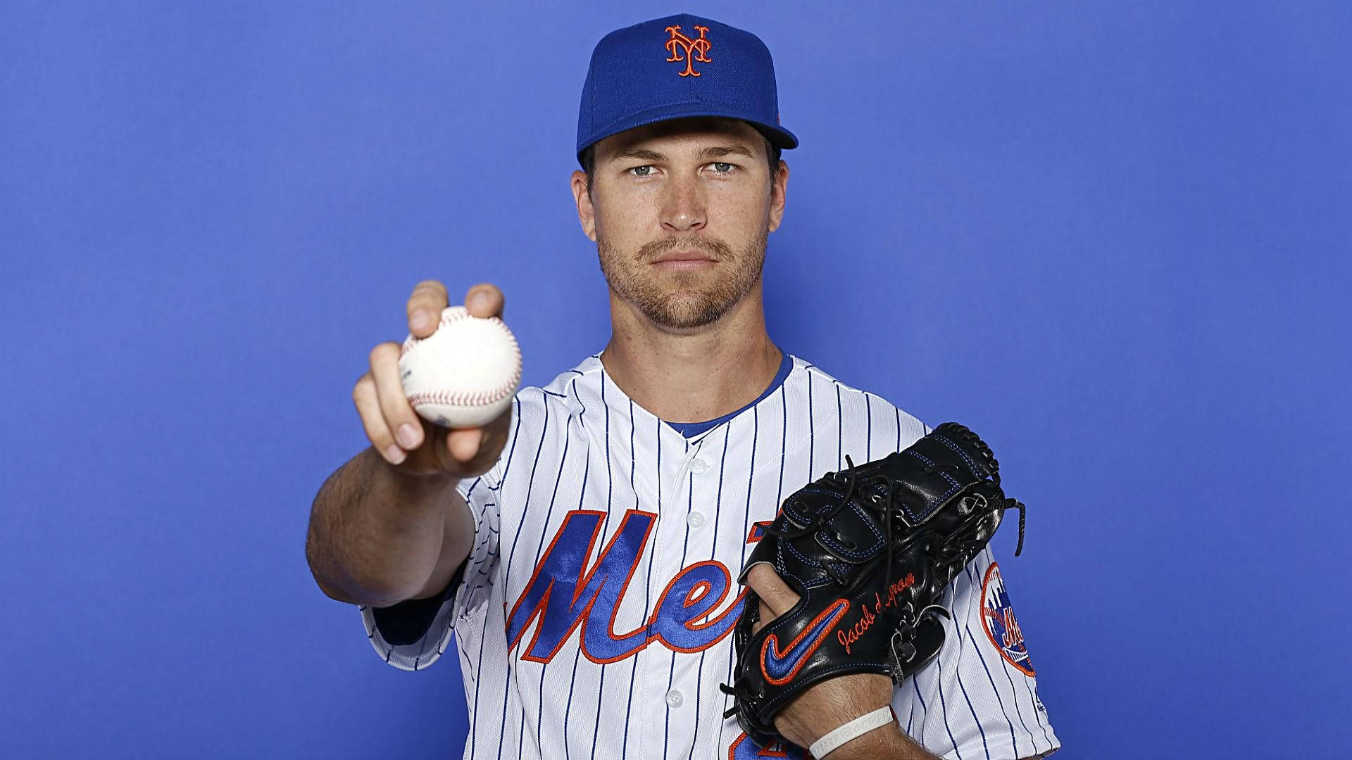 身穿大都會隊球衣的棒球運動員在藍色背景前拿著球和手套。 — MLB 壁紙