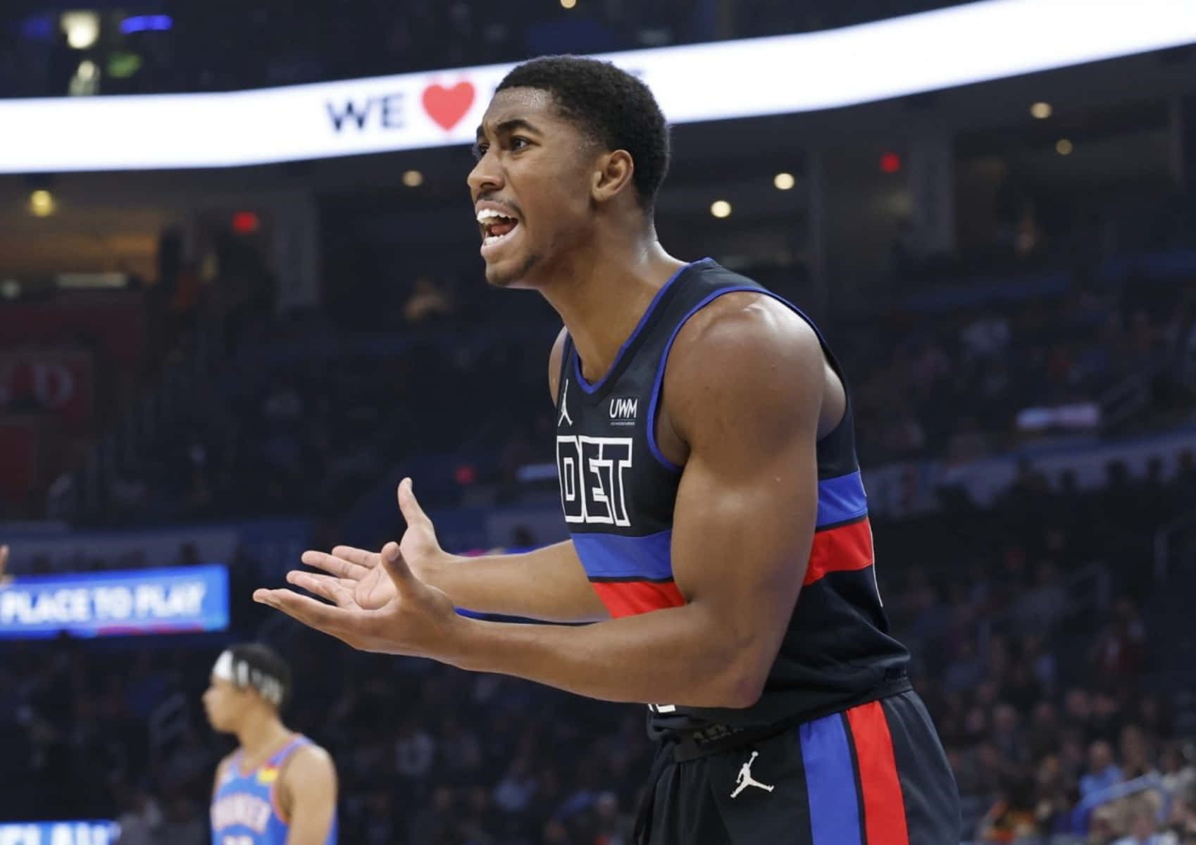 身穿活塞隊球衣的籃球運動員在比賽中做手勢，背景有觀眾。 — NBA 壁紙