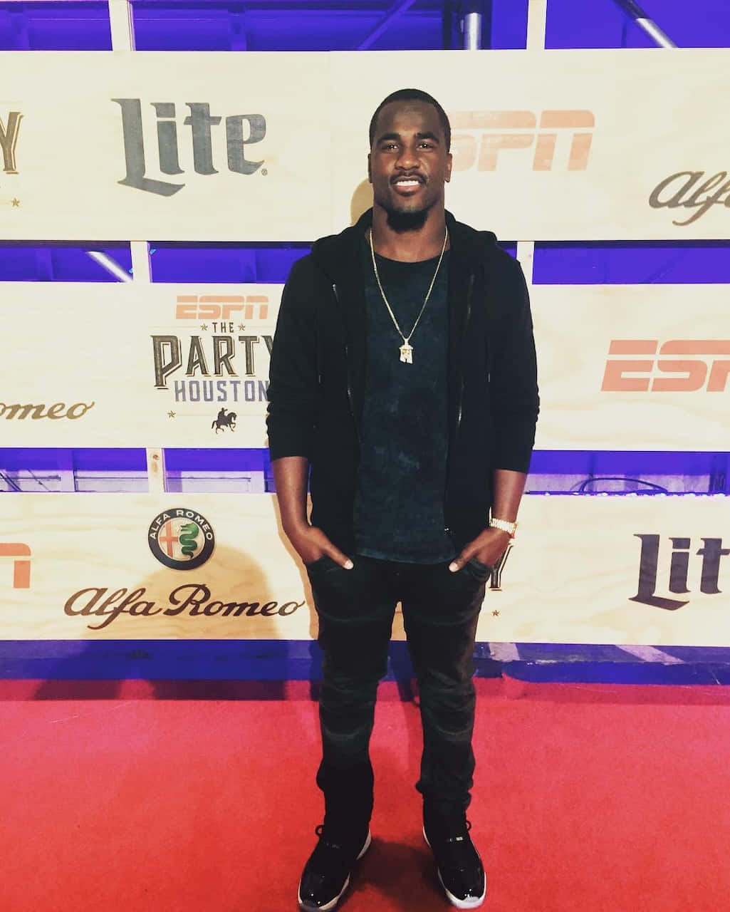  壁紙 — 一名身穿黑色連帽衫和牛仔褲的男子自信地站在ESPN品牌活動的紅地毯上，身後有標誌。