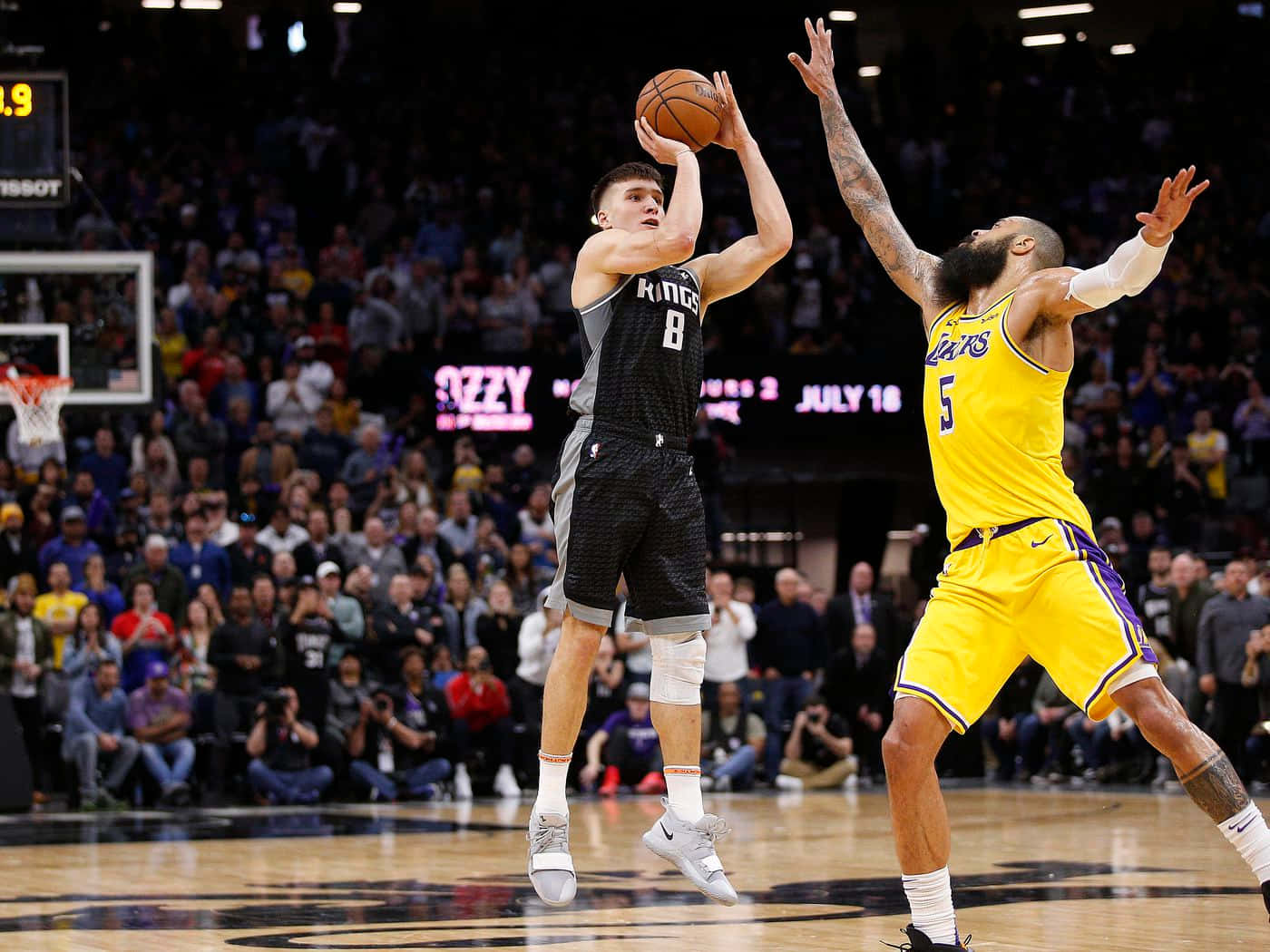 籃球運動員在擁擠的場館中越過防守者投籃。 — NBA 壁紙