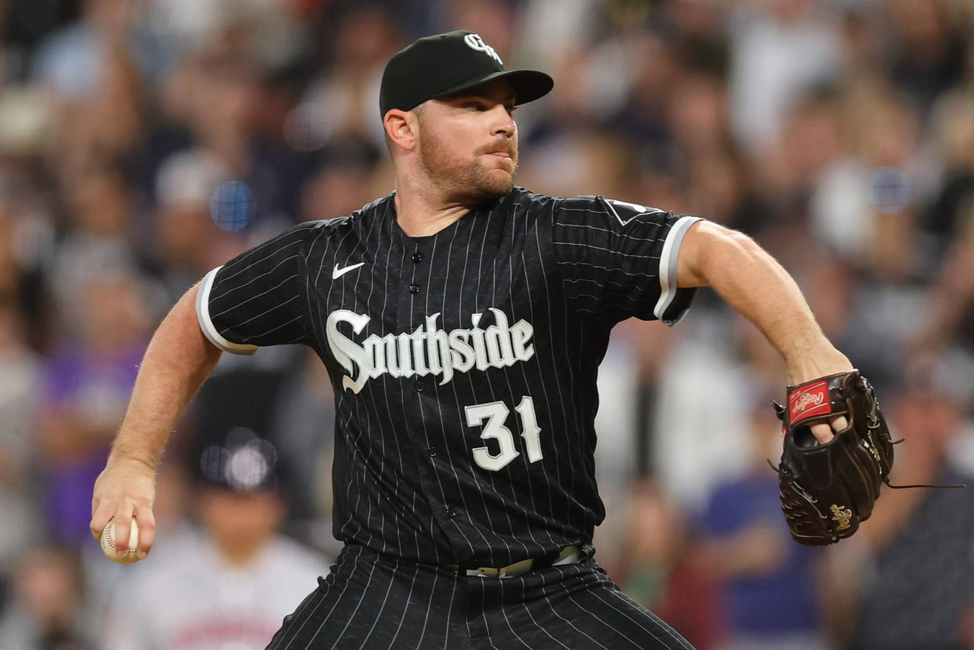 身穿黑色細條紋球衣的棒球投手在夜間比賽中投球。 — MLB 壁紙