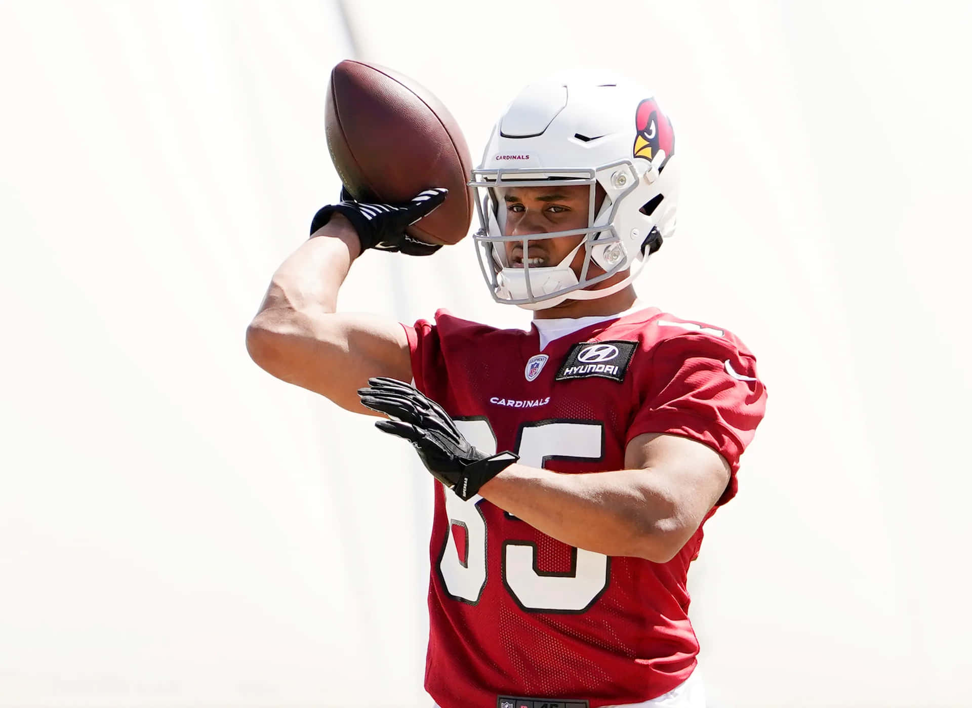  壁紙 — 一名身穿紅色 Cardinals 球衣的美式足球員正準備在明亮的白色背景下擲球。