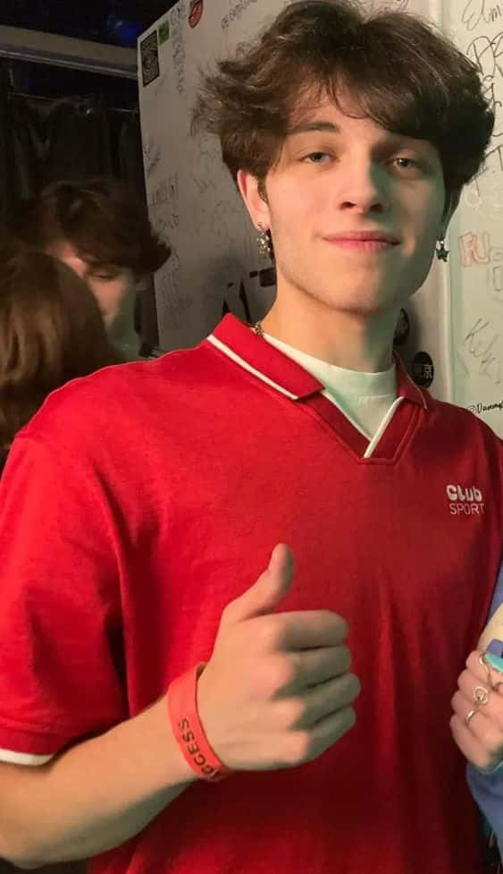  壁紙 — 一名身穿紅色Polo衫的年輕男子在一個擠滿人、牆上佈滿塗鴉的室內環境中豎起大拇指。