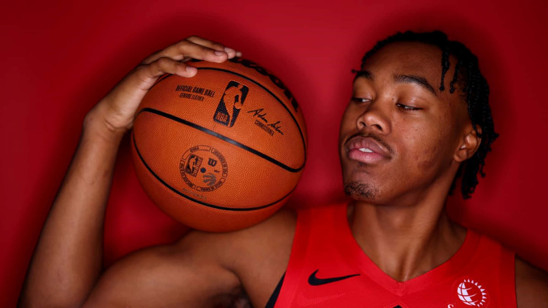 年輕籃球運動員身穿紅色球衣，在紅色背景下手持NBA比賽用球。 — NBA 壁紙