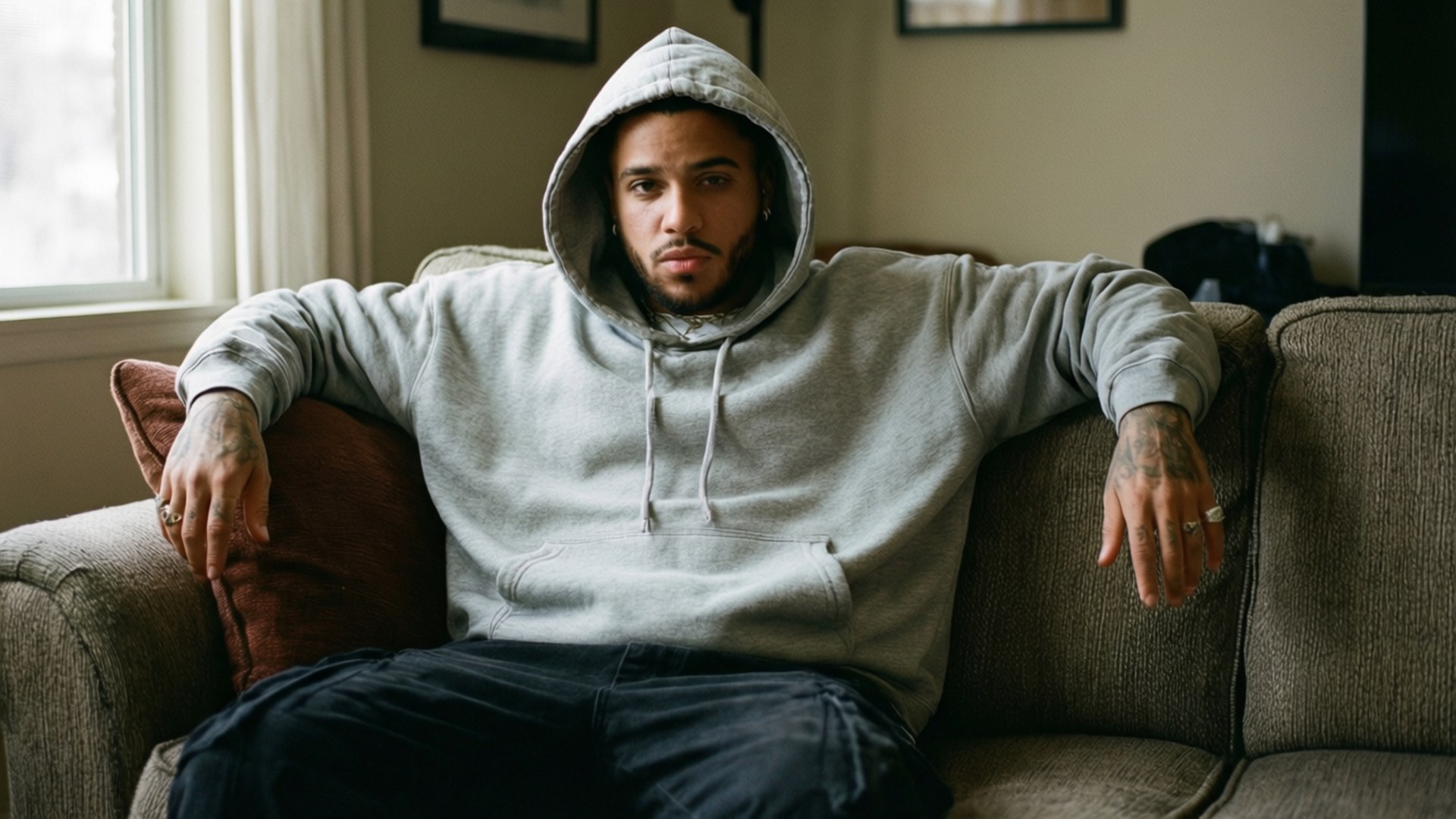 Cozy Hoodie Couch 壁紙 — 一名身穿灰色連帽衫的男子放鬆地坐在米色沙發上，雙臂擱在靠背上。