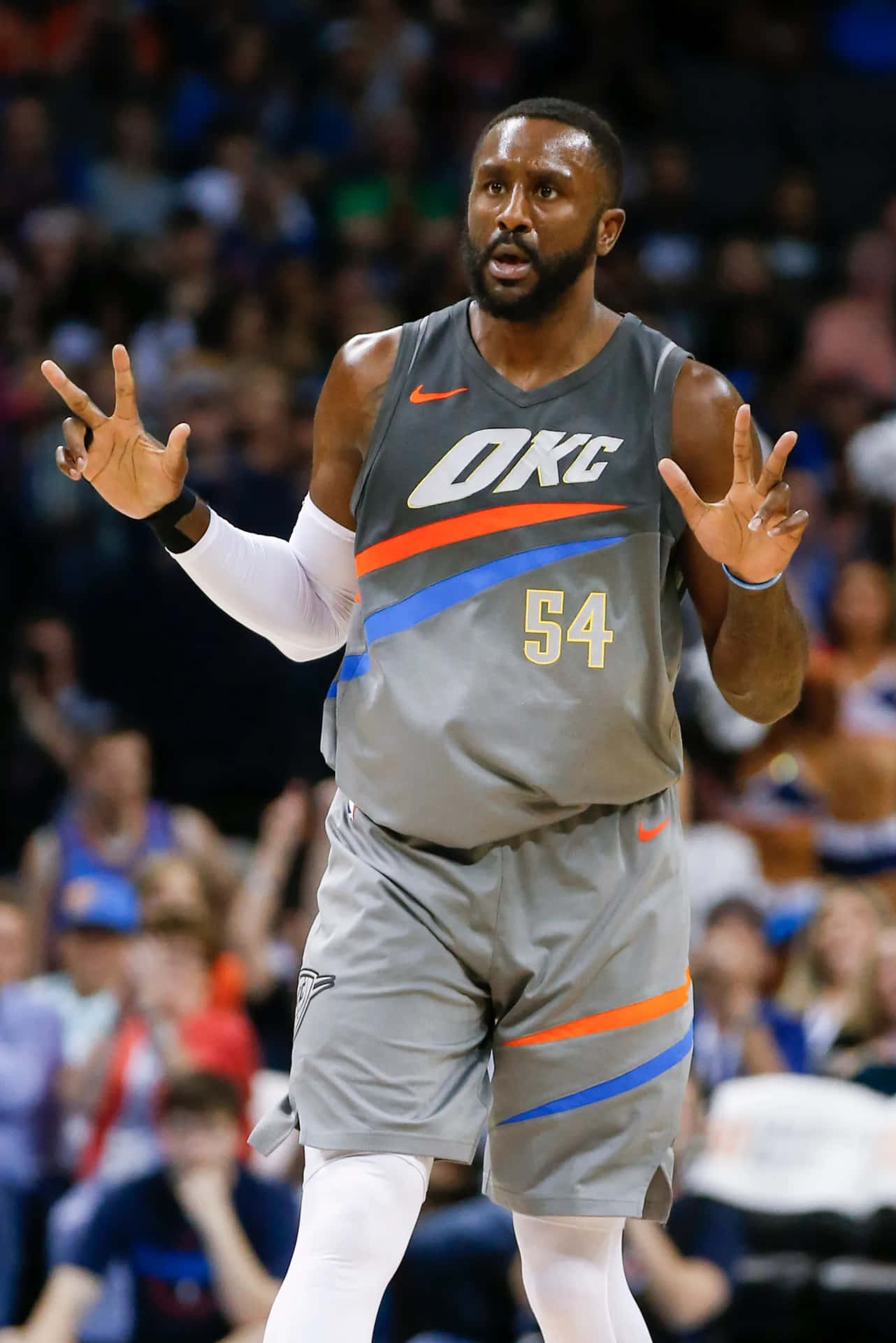  壁紙 — 一名身穿灰色OKC球衣54號的籃球運動員在場館燈光下進行激烈比賽時，雙手做出手勢。