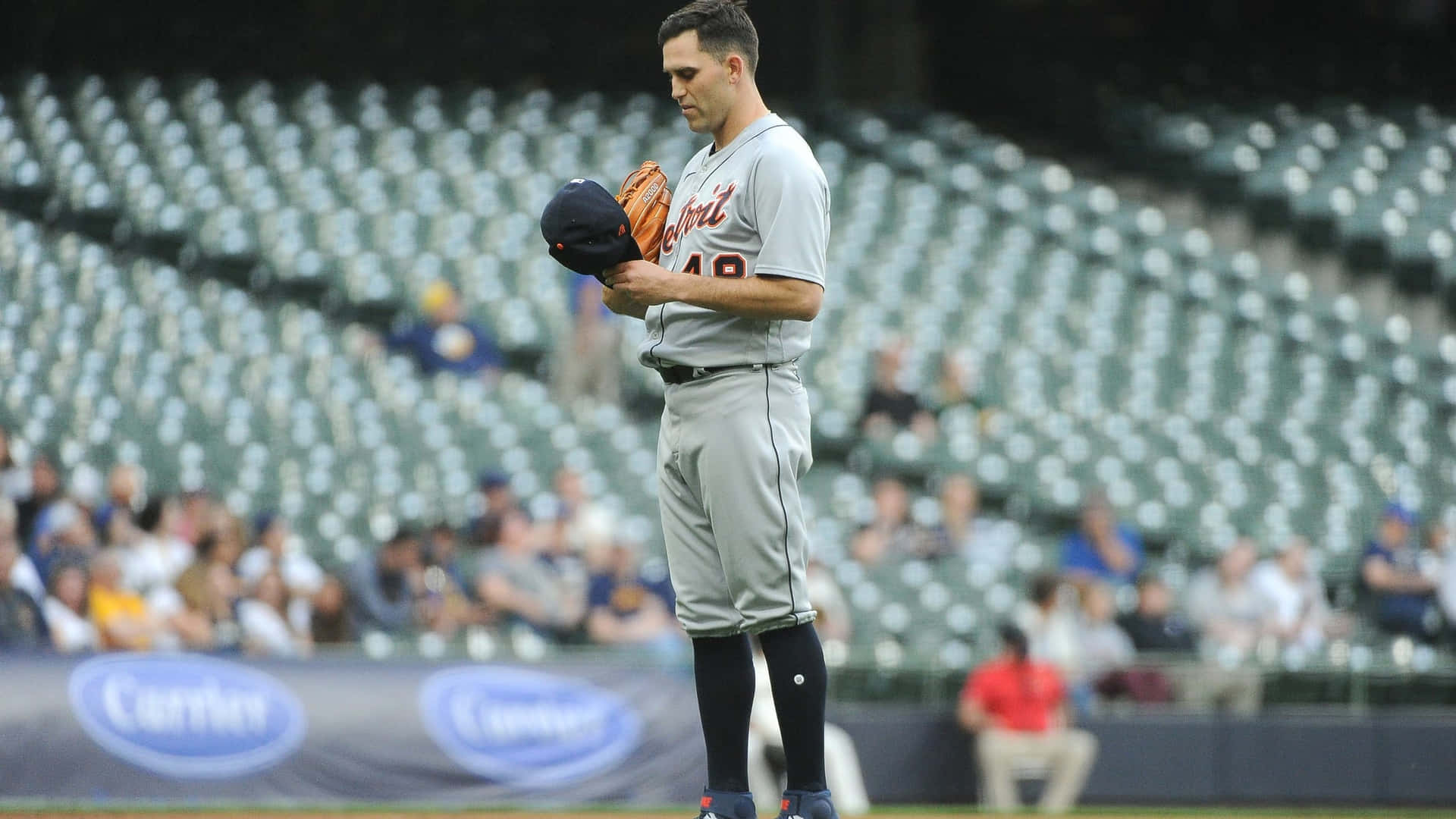 棒球投手獨自站在空蕩蕩的體育館球場上，手持帽子和手套。 — MLB 壁紙