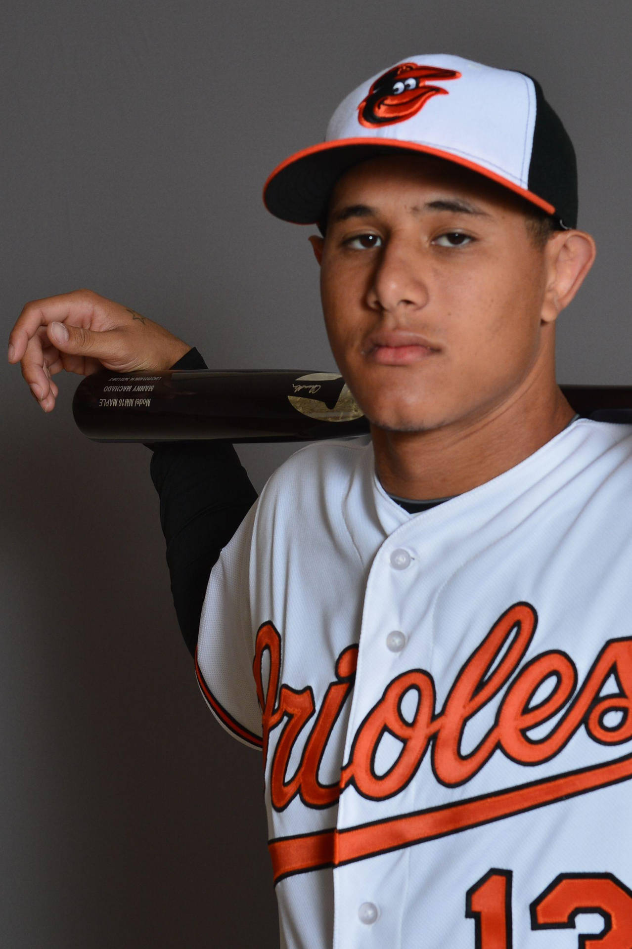 身穿金鶯隊球衣的年輕棒球運動員在攝影棚肖像中手持球棒。 — MLB 壁紙