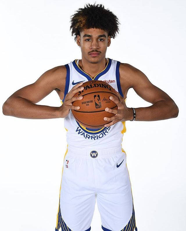 身穿金州勇士隊球衣的年輕籃球運動員拿著一個籃球。 — NBA 壁紙