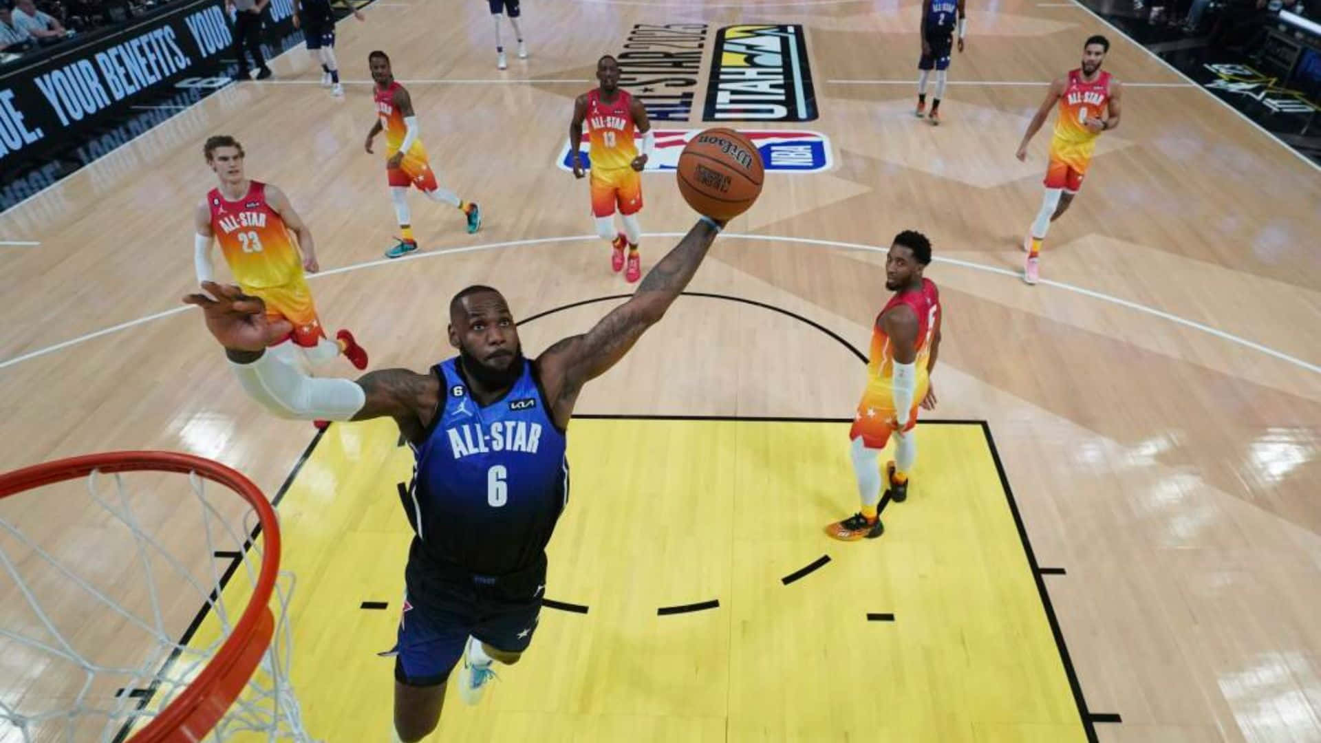 NBA Game 桌布 壁紙 — 一名身穿藍色全明星球衣的籃球運動員在場上大力灌籃，身穿橙色球衣的對手在場邊觀看。