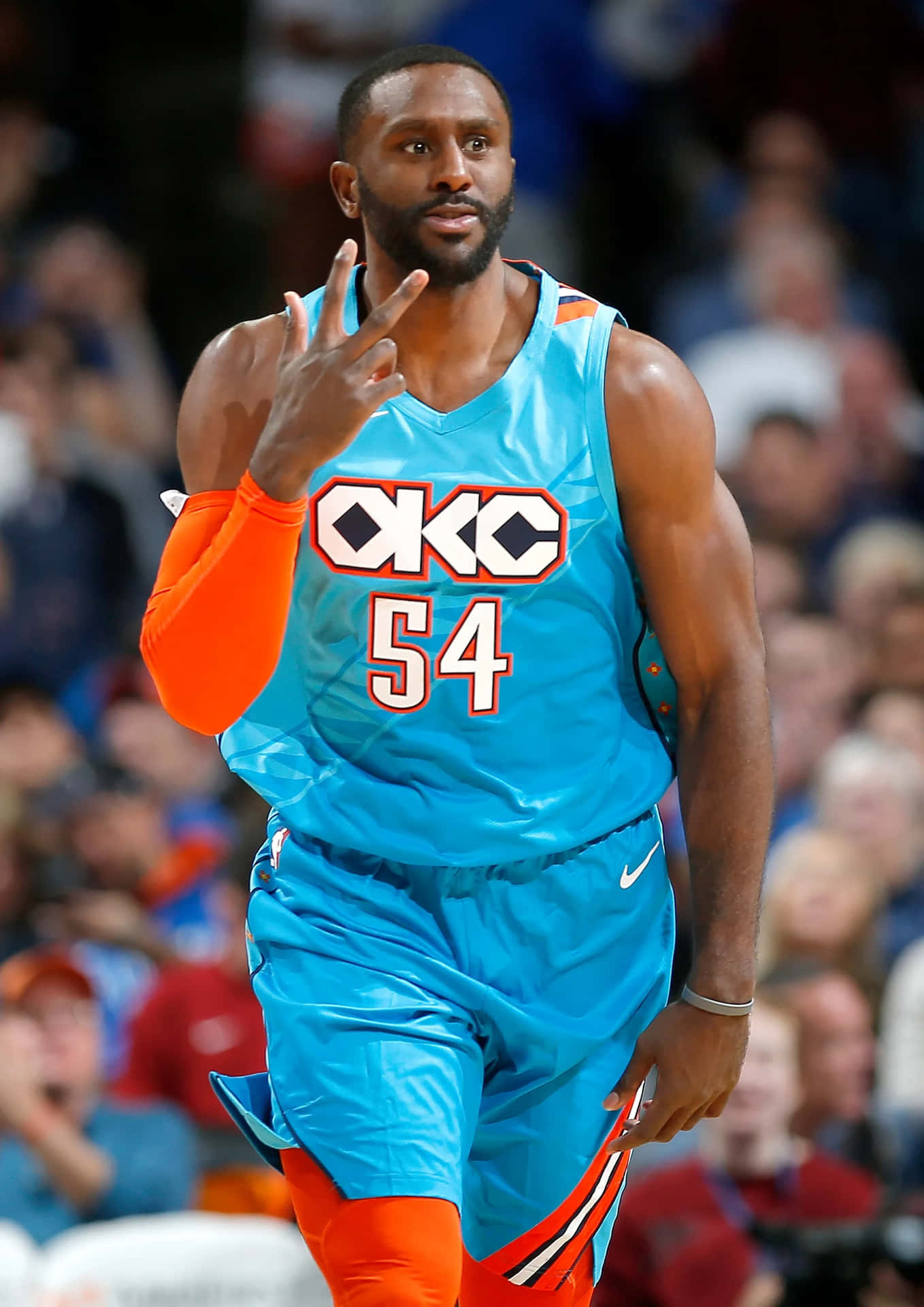  壁紙 — 一名身穿亮藍色和橙色OKC球衣54號的籃球運動員在比賽中做出和平手勢。
