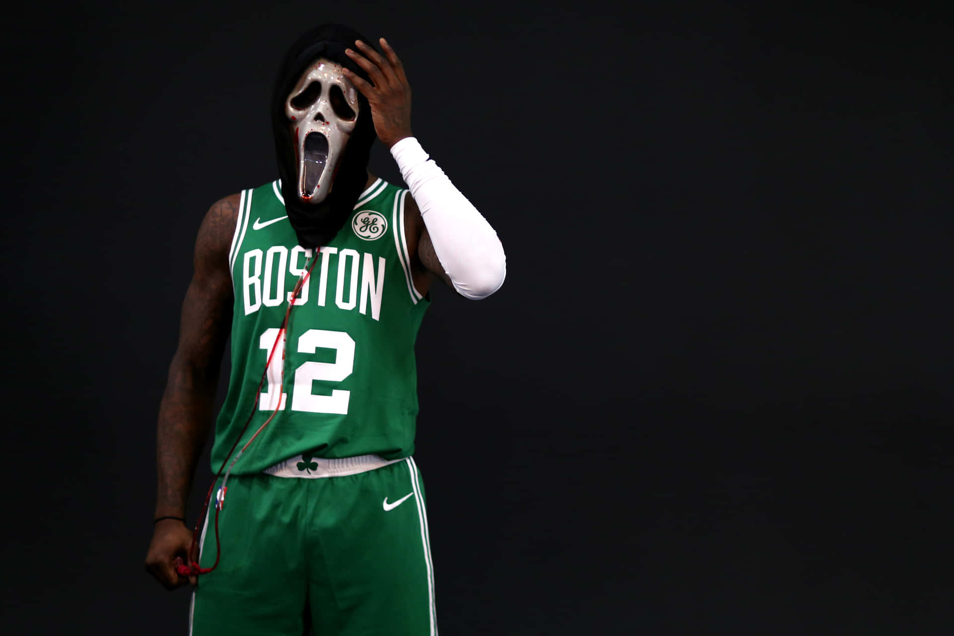 身穿綠色波士頓球衣的籃球運動員戴著Ghostface面具托著頭。 — NBA 壁紙