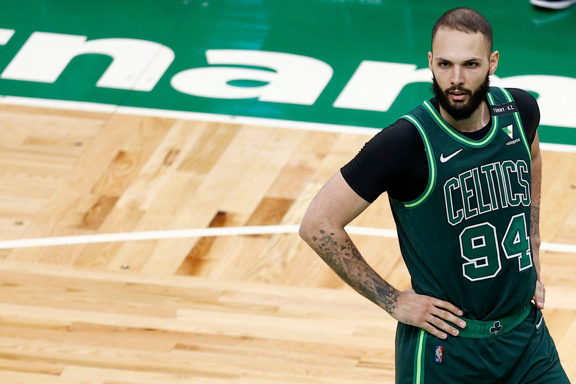 身穿綠色塞爾提克球衣的籃球運動員站在木地板上，雙手叉腰。 — NBA 壁紙
