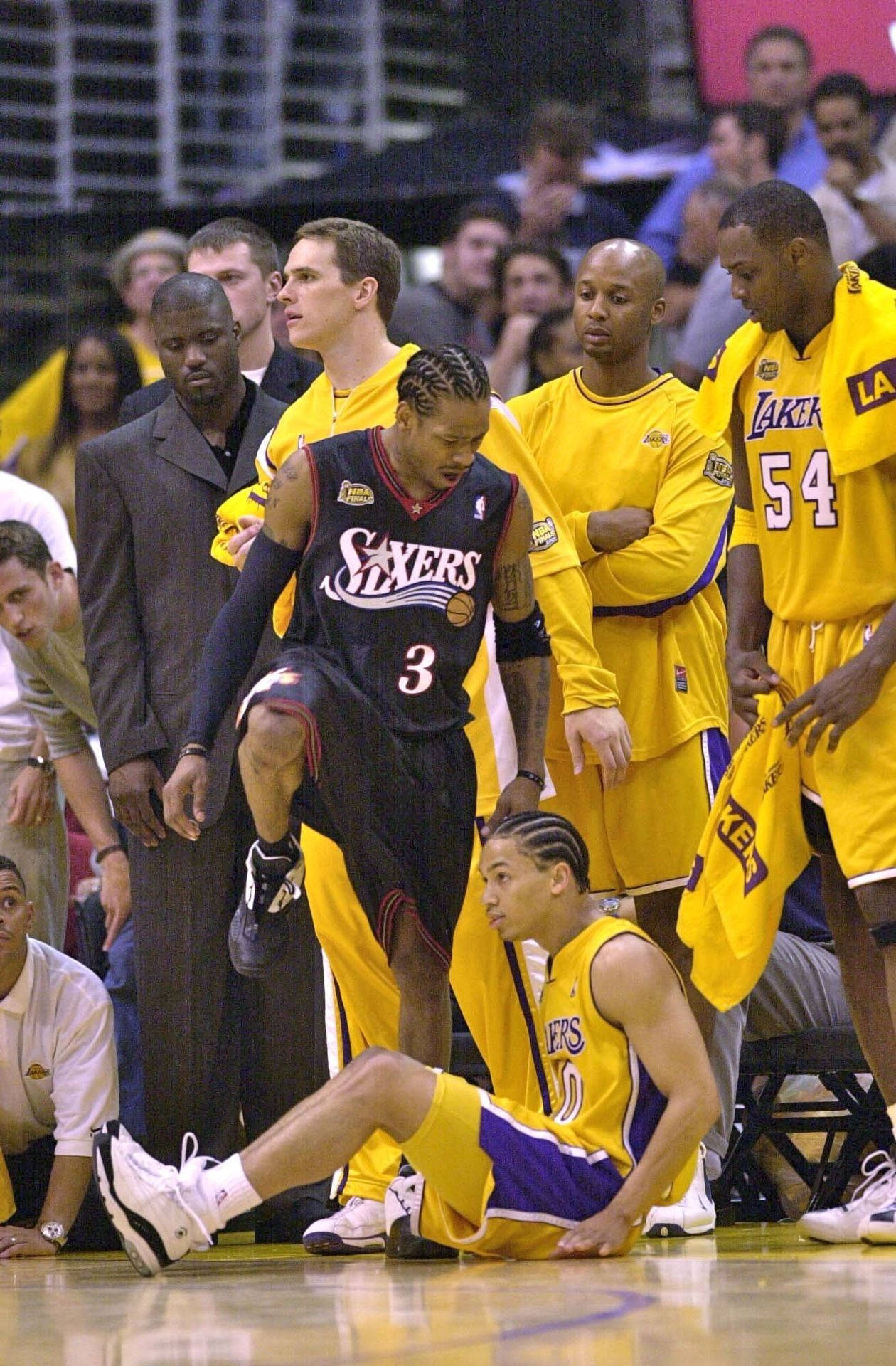 身穿Sixers球衣的籃球運動員在比賽中站在倒地的Lakers球員上方。 — NBA 壁紙