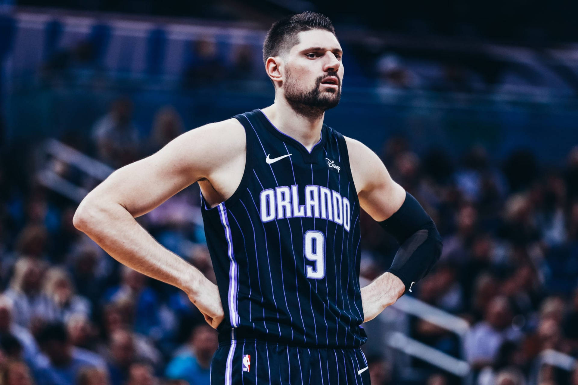 身穿奧蘭多球衣的籃球運動員比賽期間雙手叉腰站立。 — NBA 壁紙